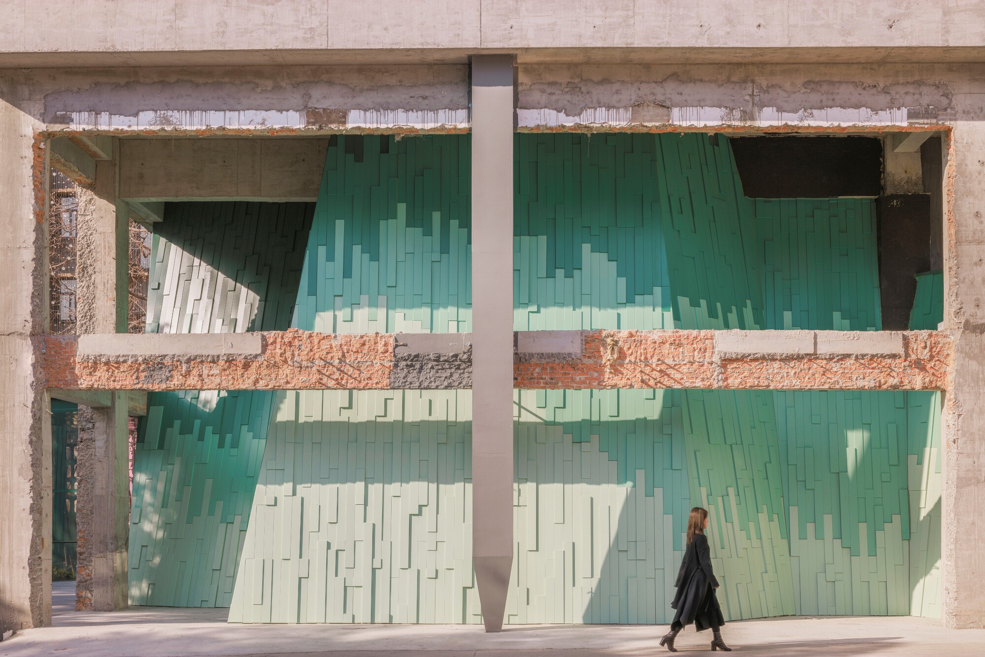 Concrete frame enclosing pixelated green tile screens as a person walks past on the sidewalk