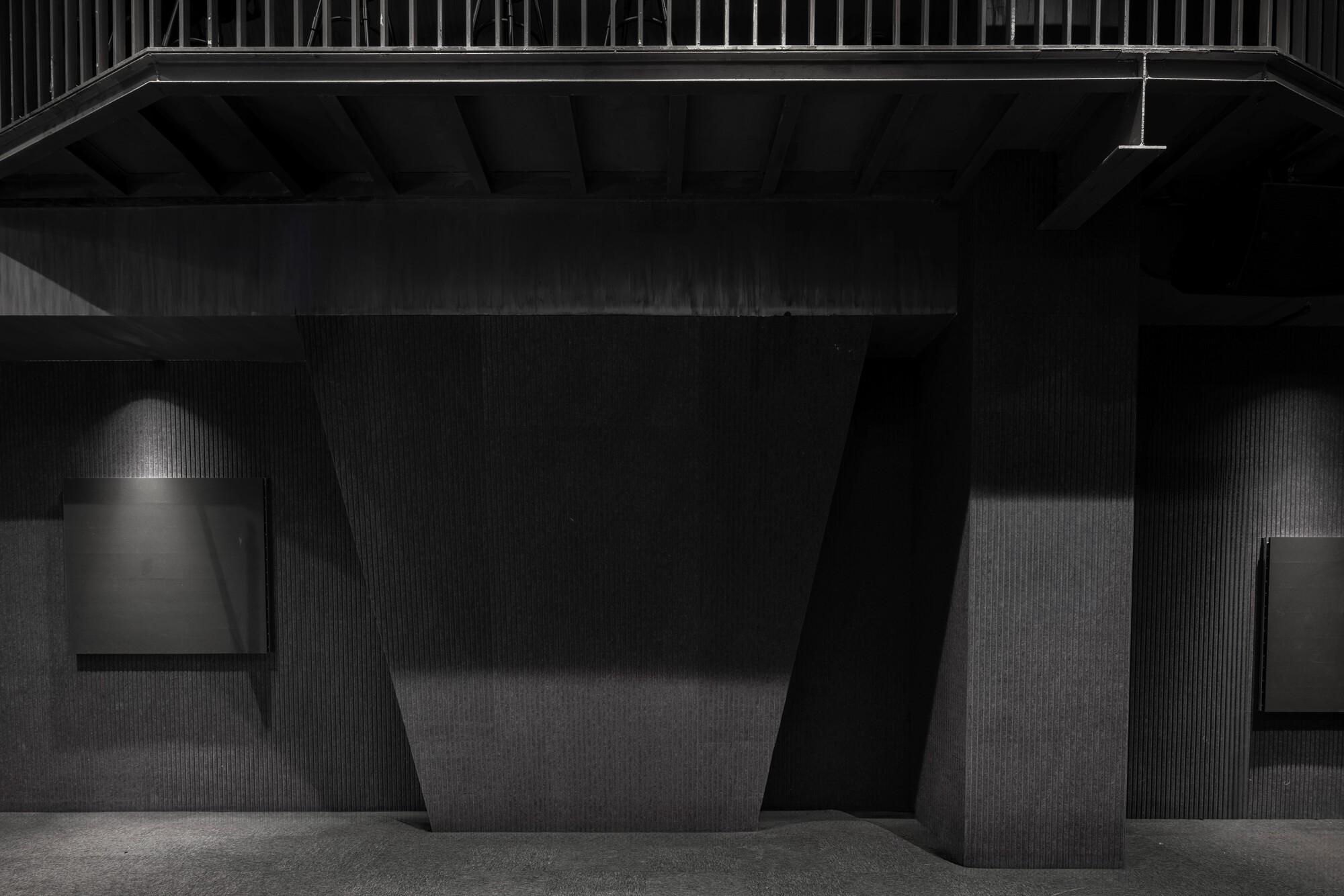 Dark ribbed wall panels flanking a central void with angled structural beams and pendant light