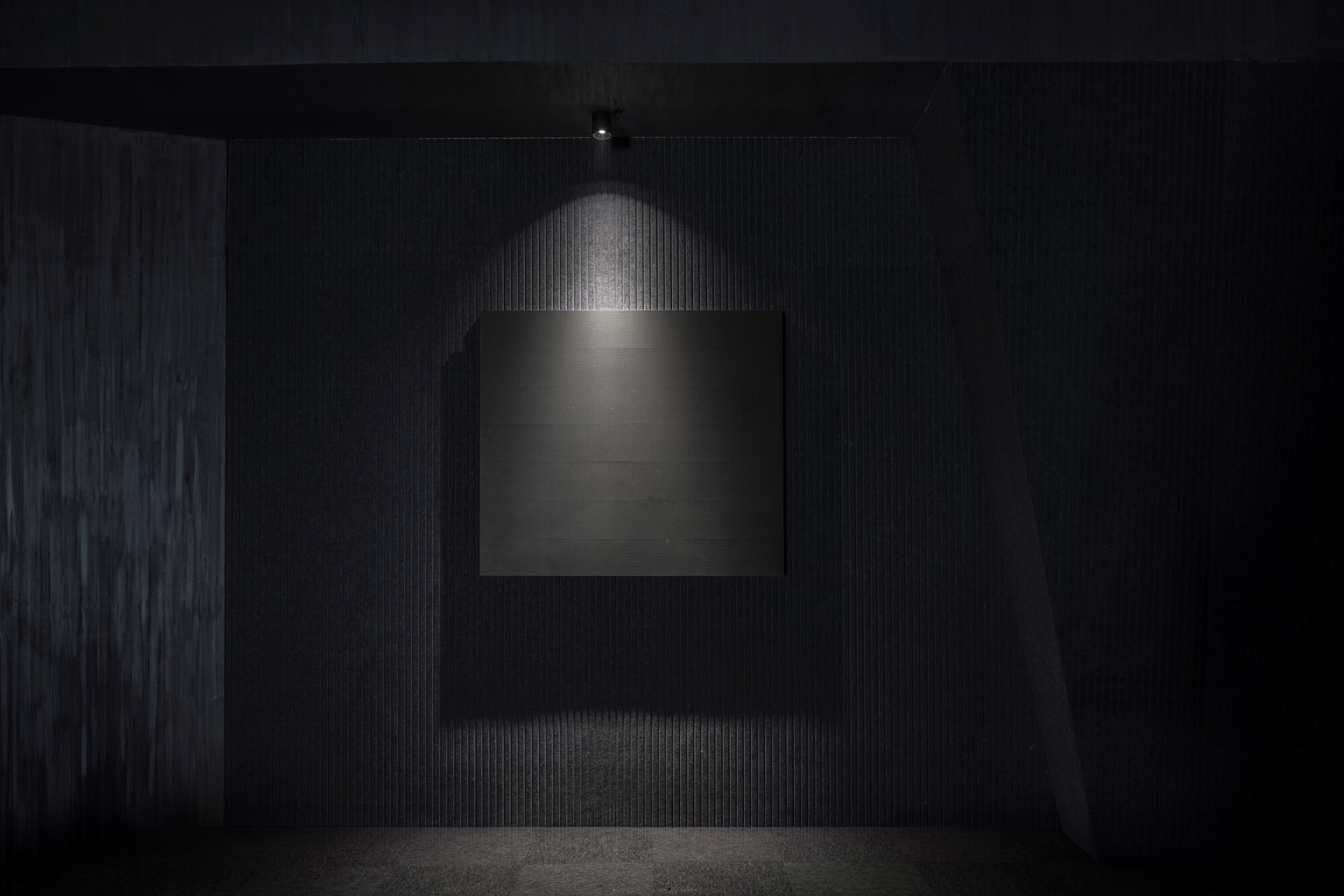 Illuminated display niche framed by black ribbed wall surfaces under a single pendant light