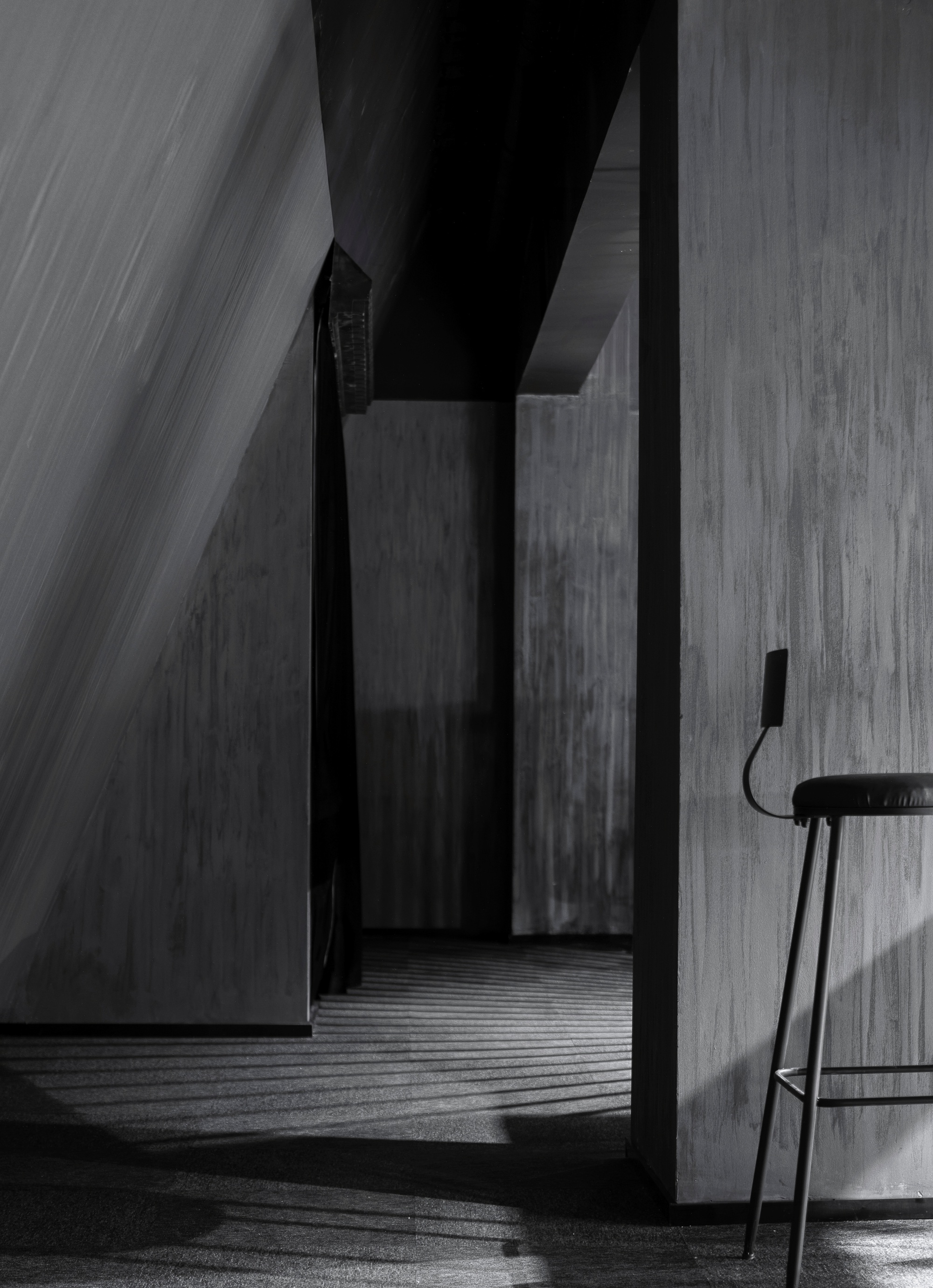 Narrow concrete corridor with angled walls and sharp daylight casting striped shadows across the floor