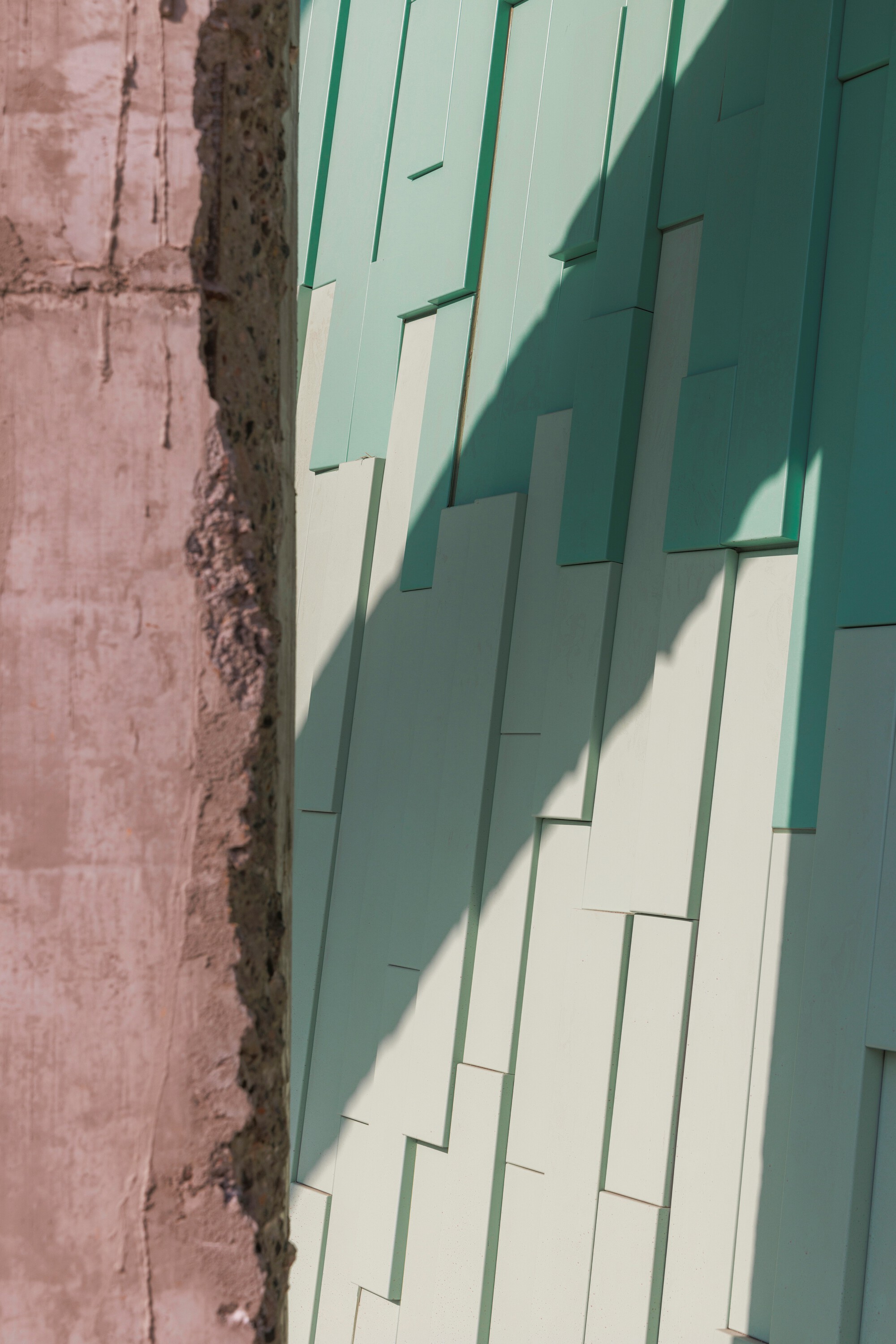 Layered mint green facade panels with shadow play against an exposed mortar and concrete edge