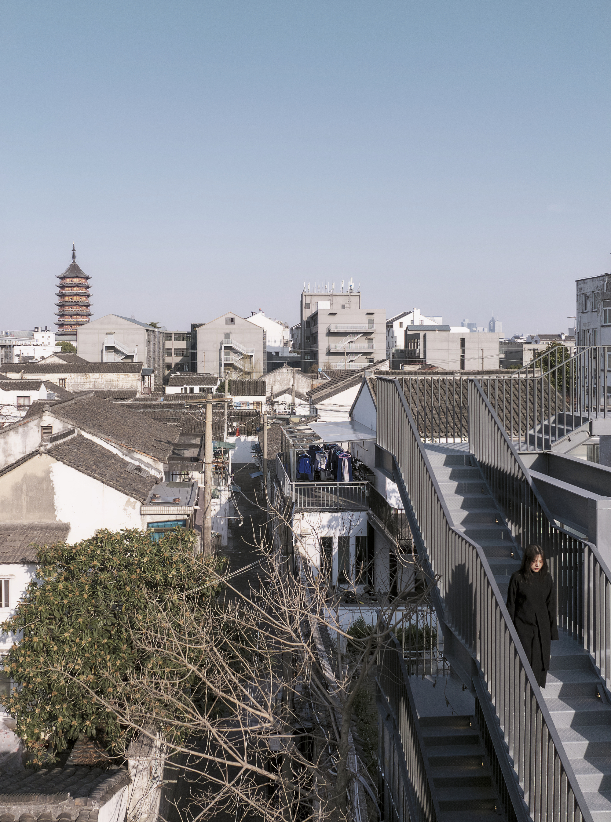 Elevated walkway with metal railings overlooking traditional rooftops and a pagoda tower in the distance