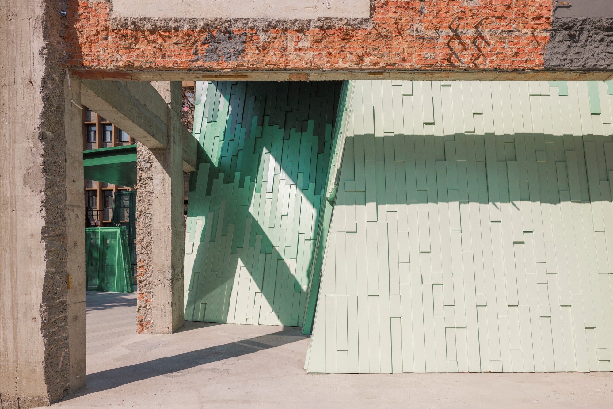Interior passage through exposed brick and concrete frame with sunlight casting shadows on the glass tiles
