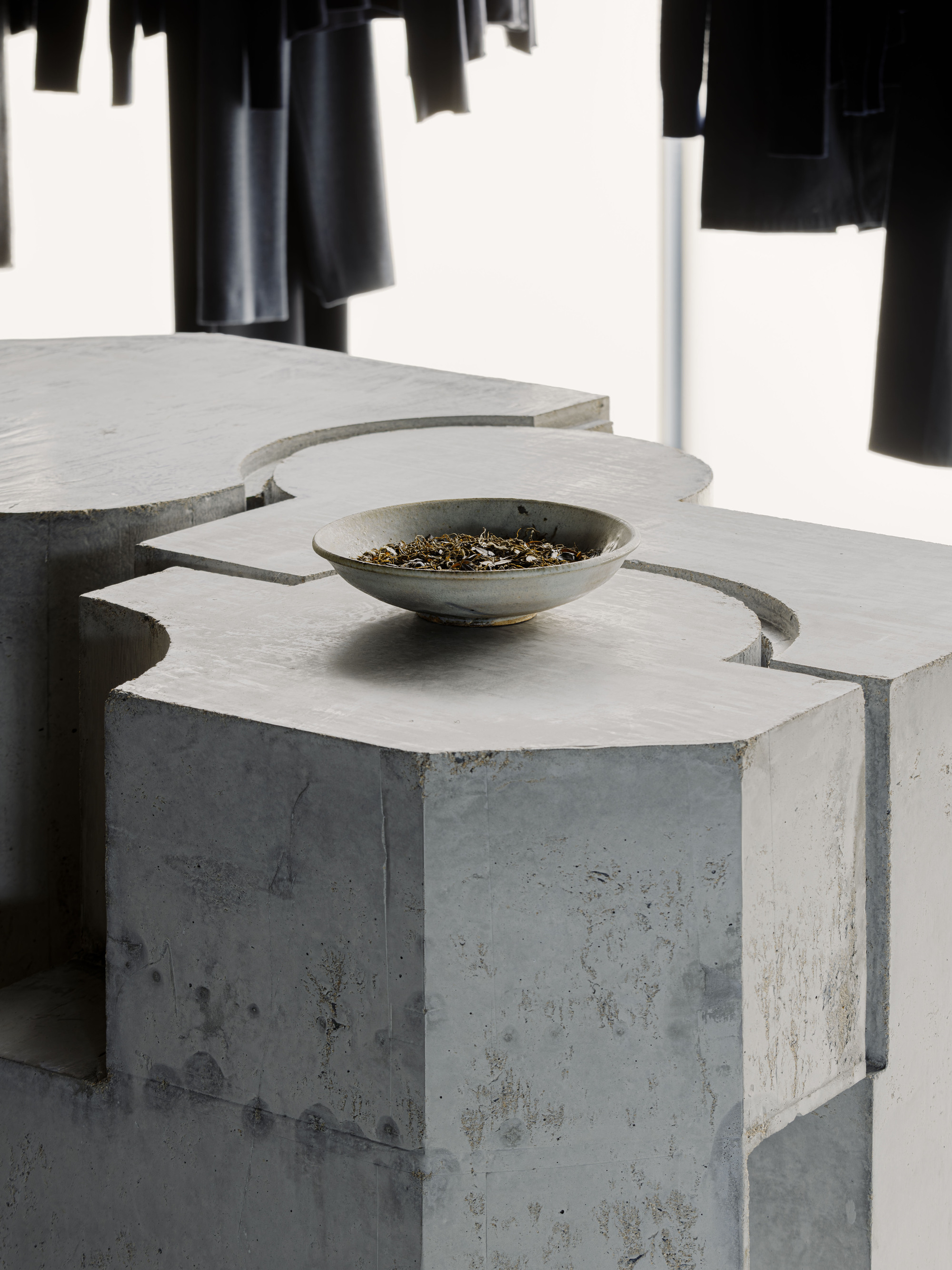 Close-up of a ceramic bowl resting on an interlocking concrete volume with chamfered edges