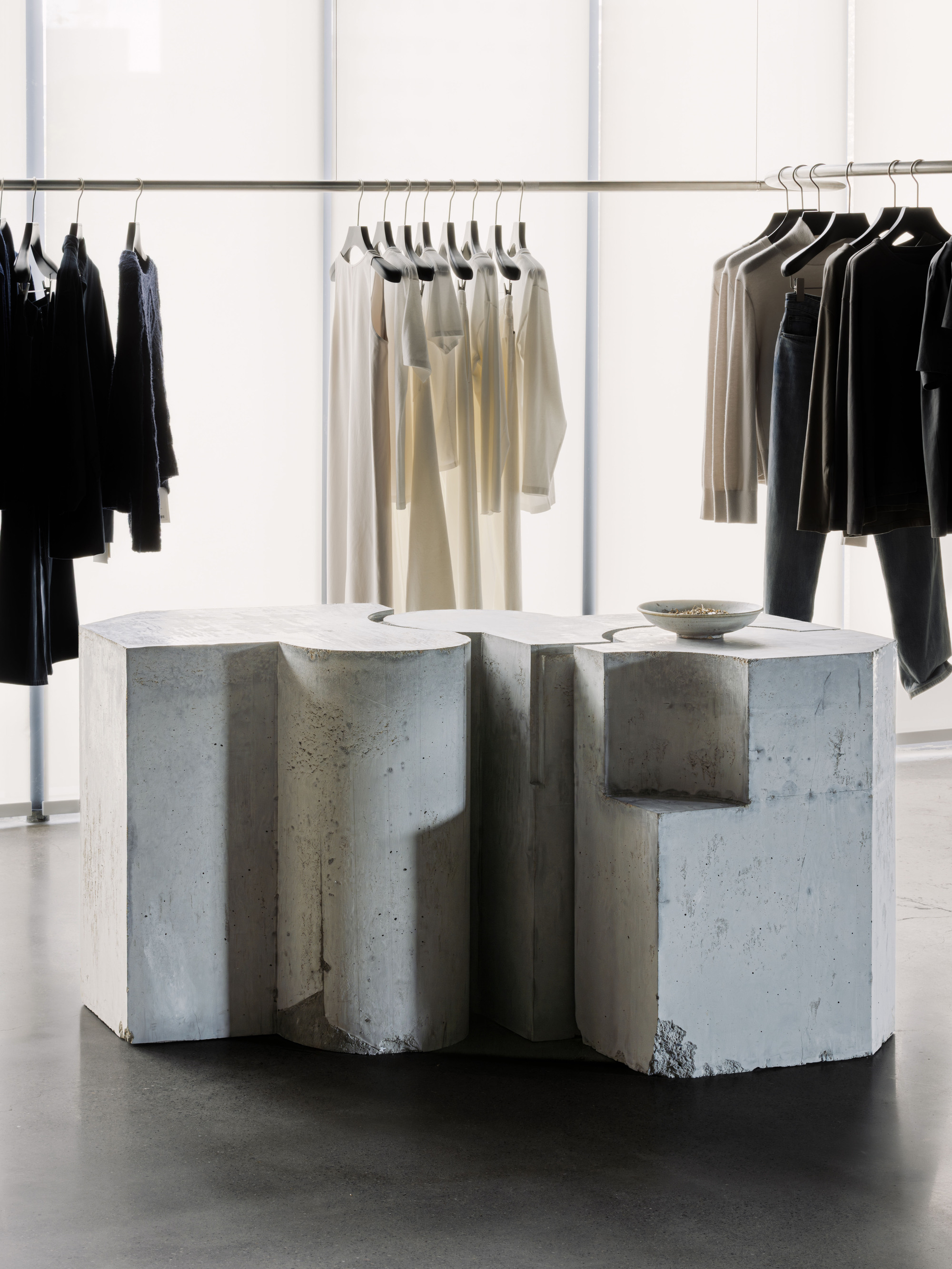 Cast concrete display counter with undulating faceted surfaces beneath hanging garments in a retail interior