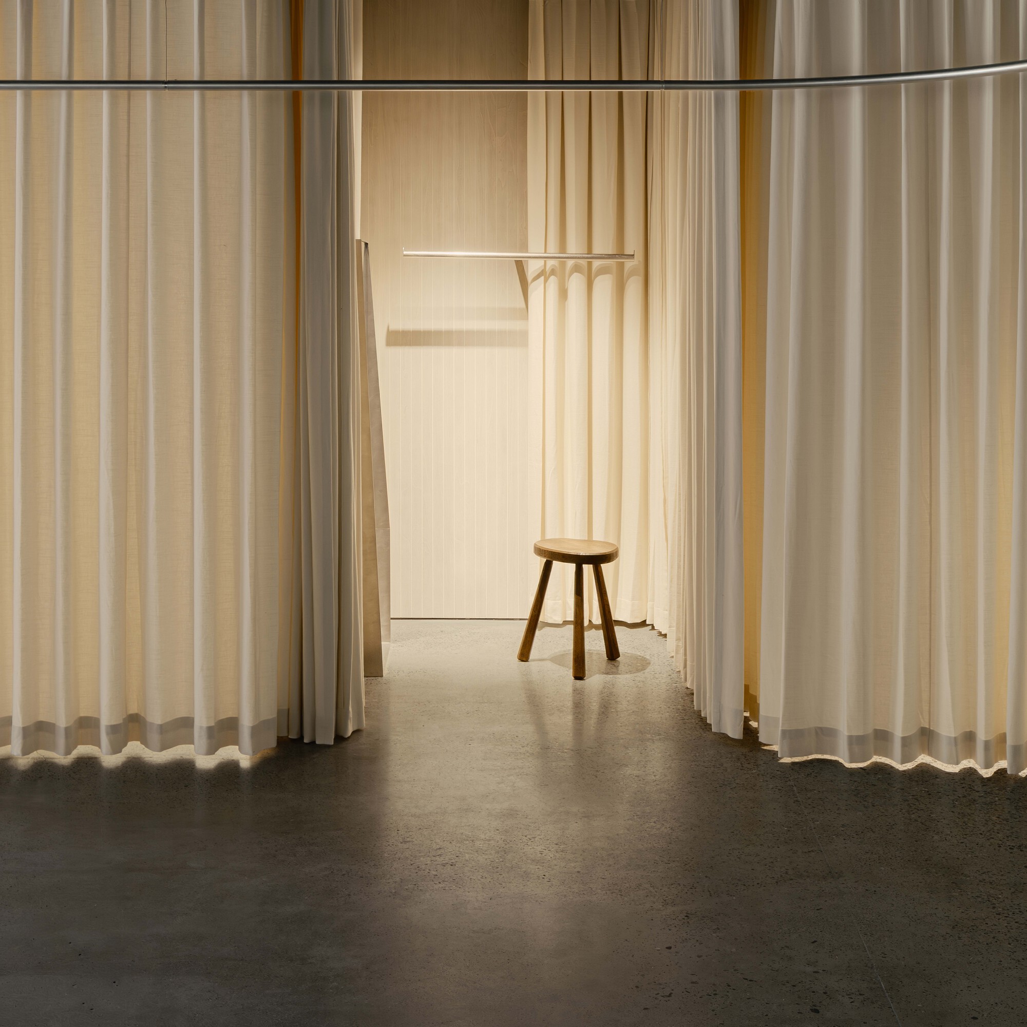 Corridor framed by hanging curtains leading to a wooden stool and coat rack
