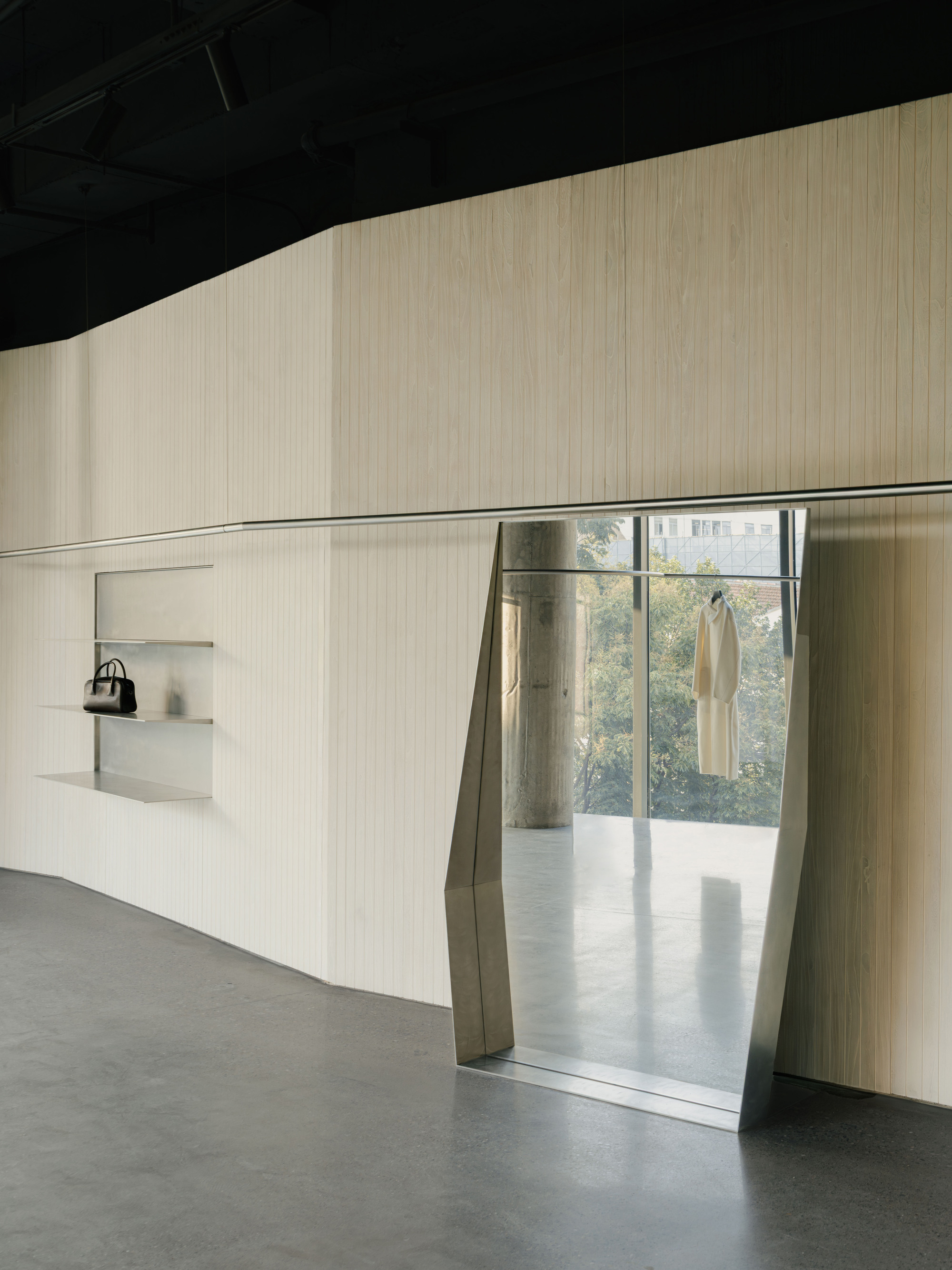 Angled doorway cut through ribbed wall with metal surround leading to daylit space beyond