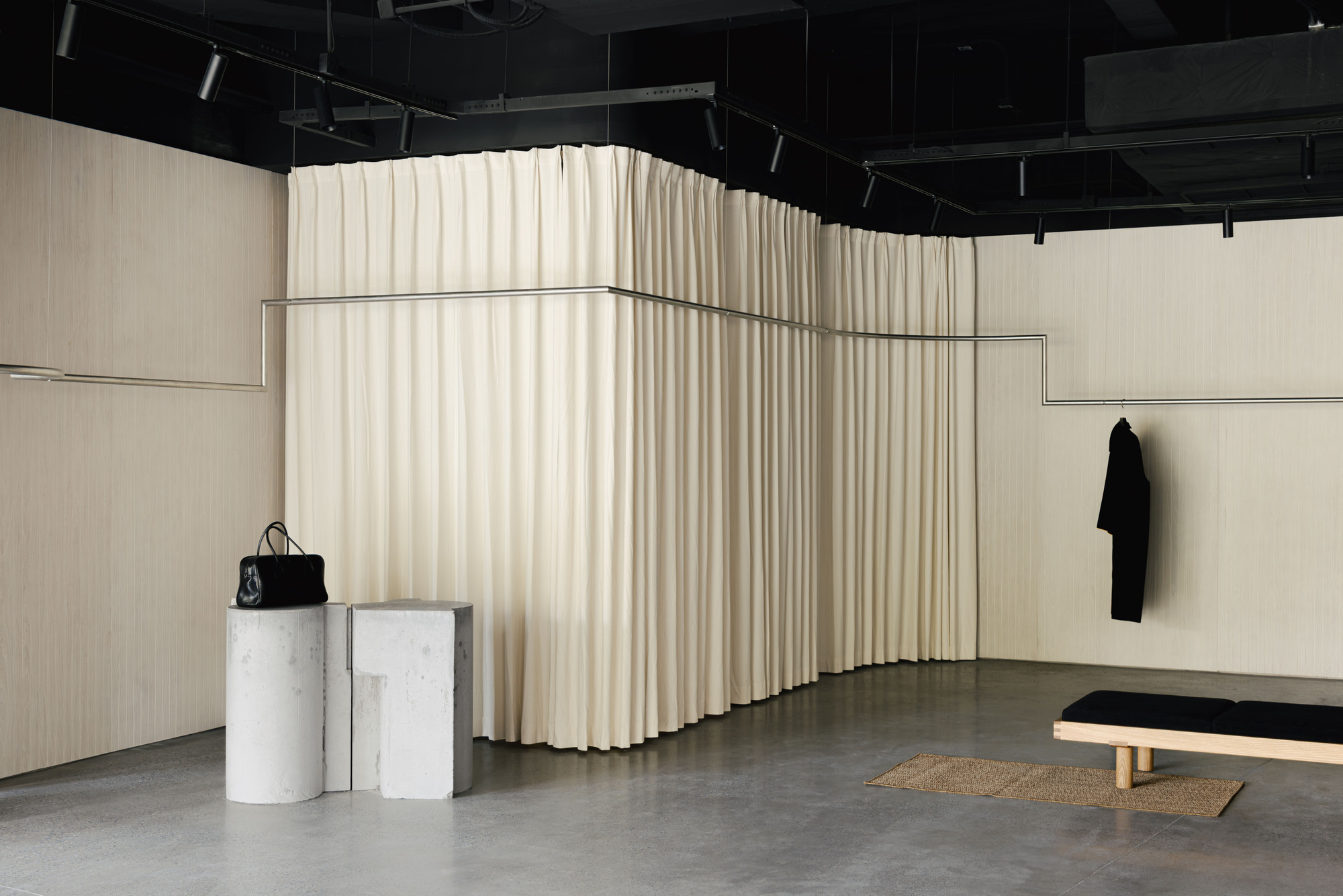Retail interior with pleated cream curtain dividers, concrete pedestals and exposed black ceiling grid