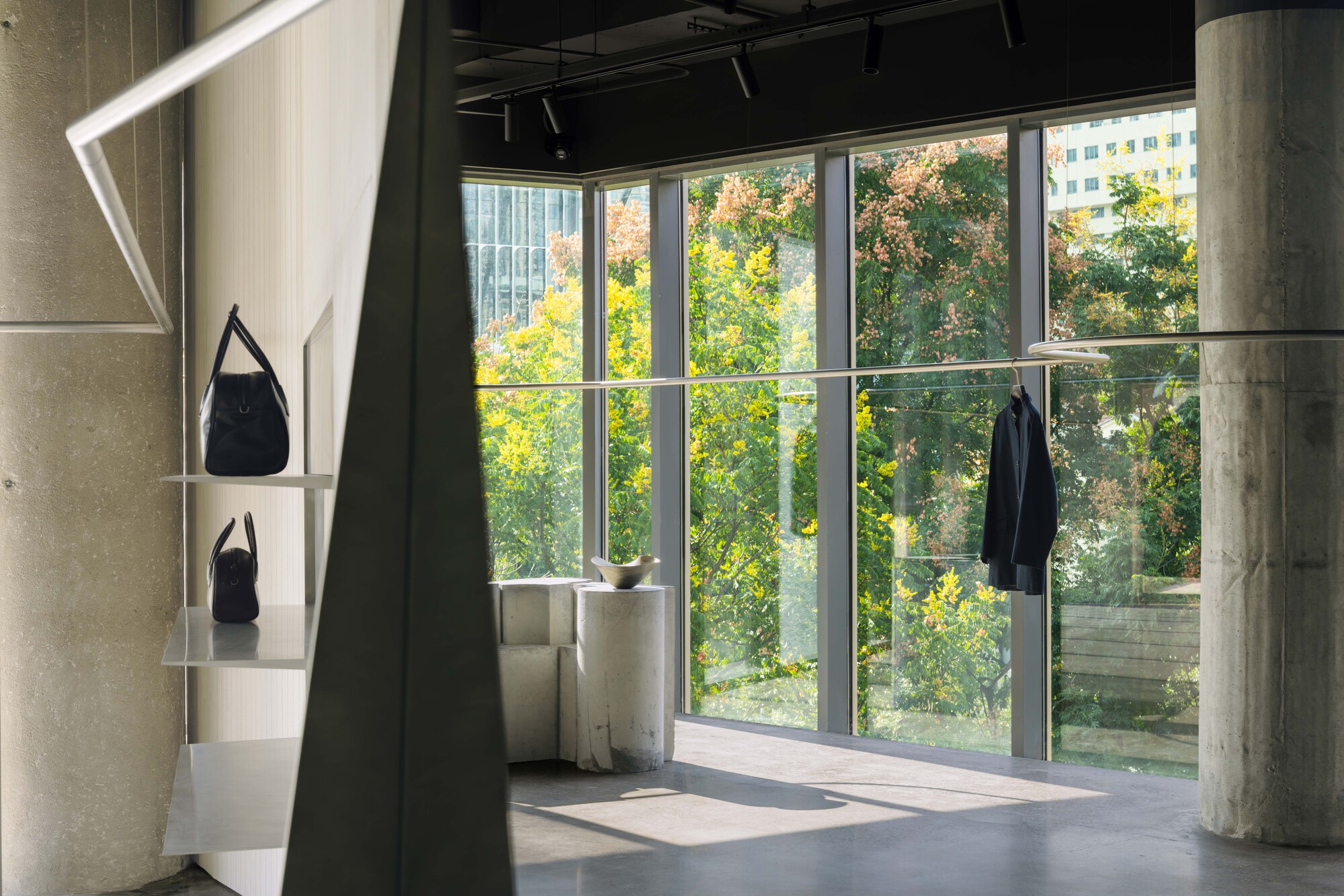 Floor-to-ceiling glazing framing autumn trees beyond exposed concrete columns and dark curtain