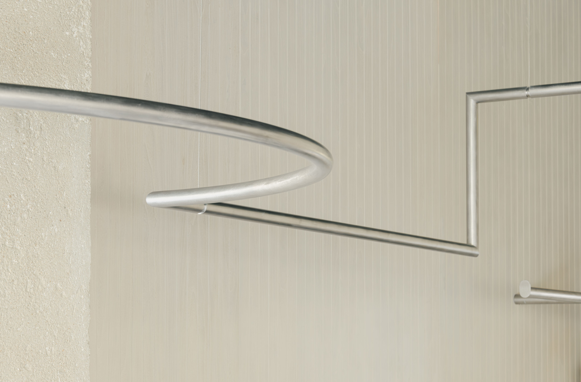 Detail of curved and straight metal clothing rails against textured light-colored wall panels
