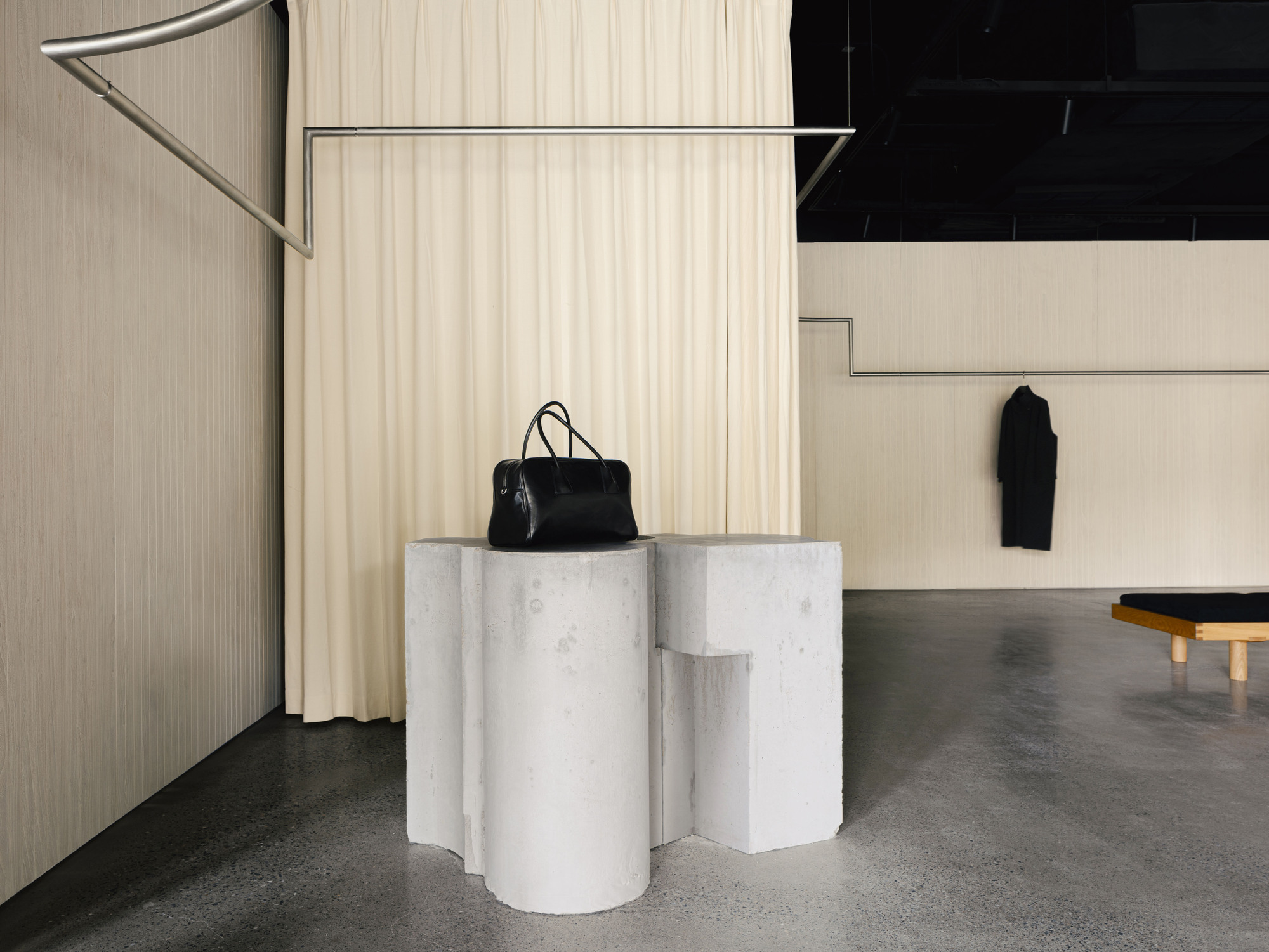 White marble cylinder display plinths with a black bag beneath metal rails and sheer curtains