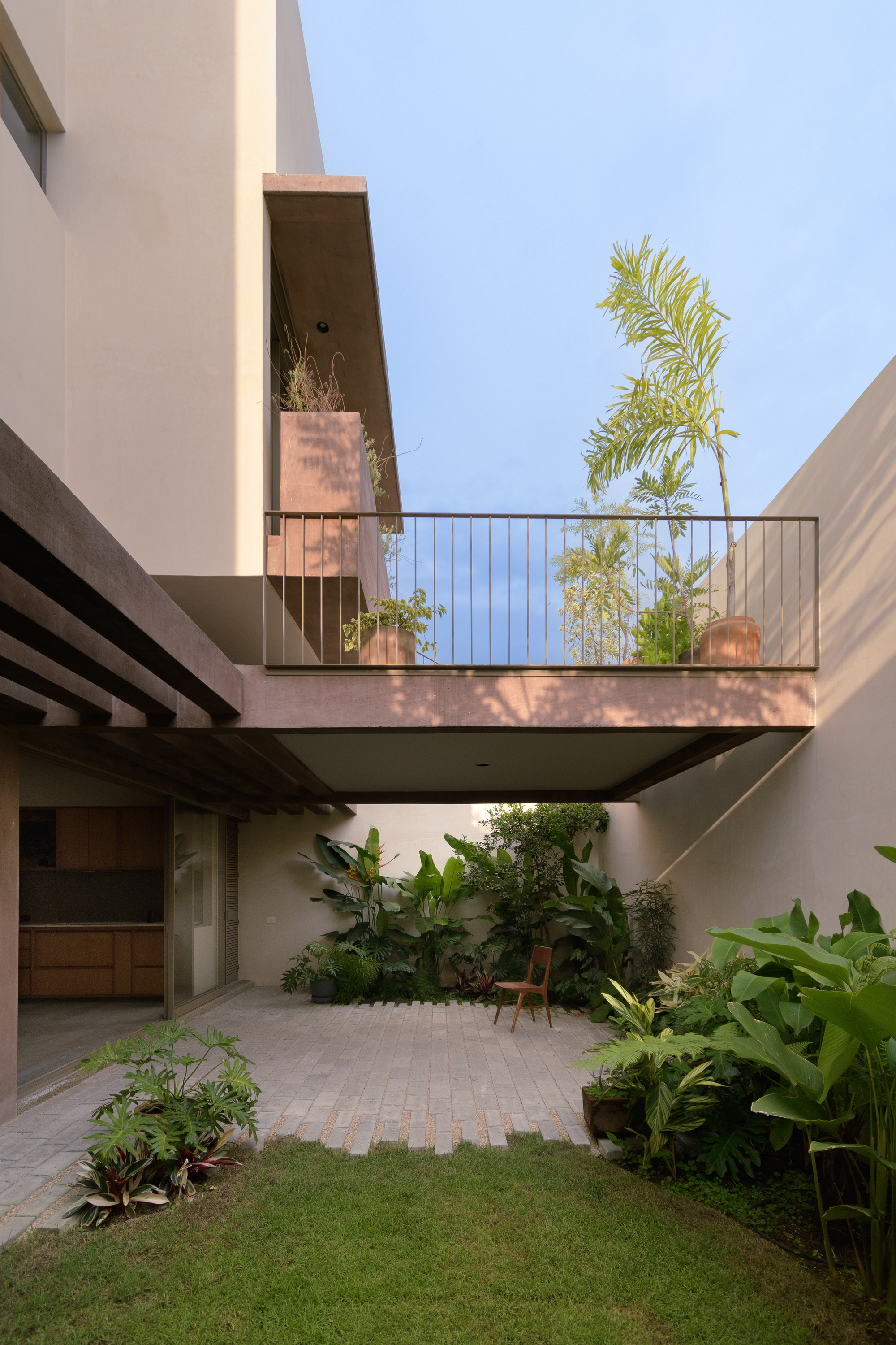 Courtyard view showing cantilevered upper terrace with metal railing and potted palms against clear sky