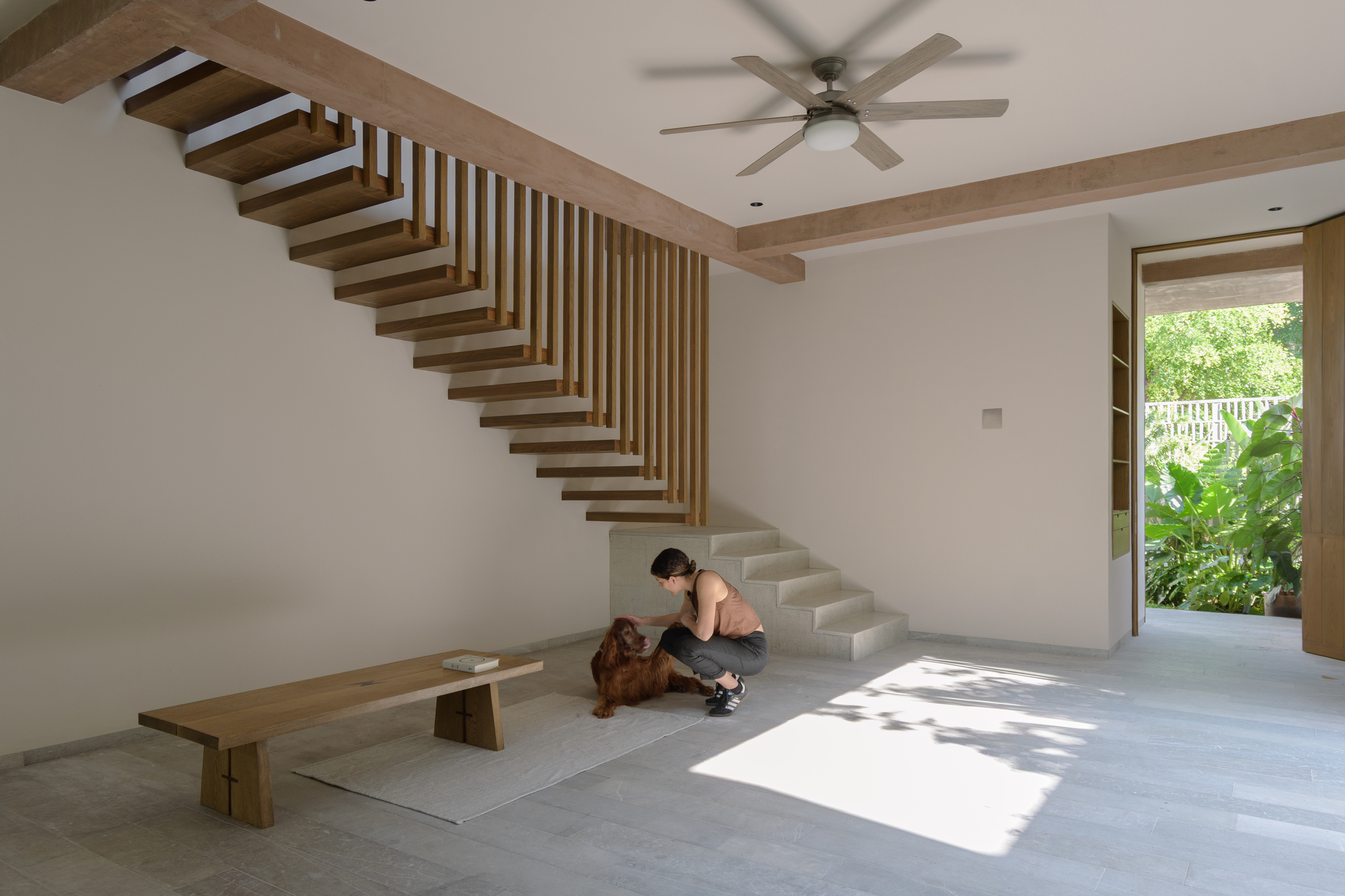 Cantilevered timber staircase with vertical slat balustrade in double-height space with person seated on floor