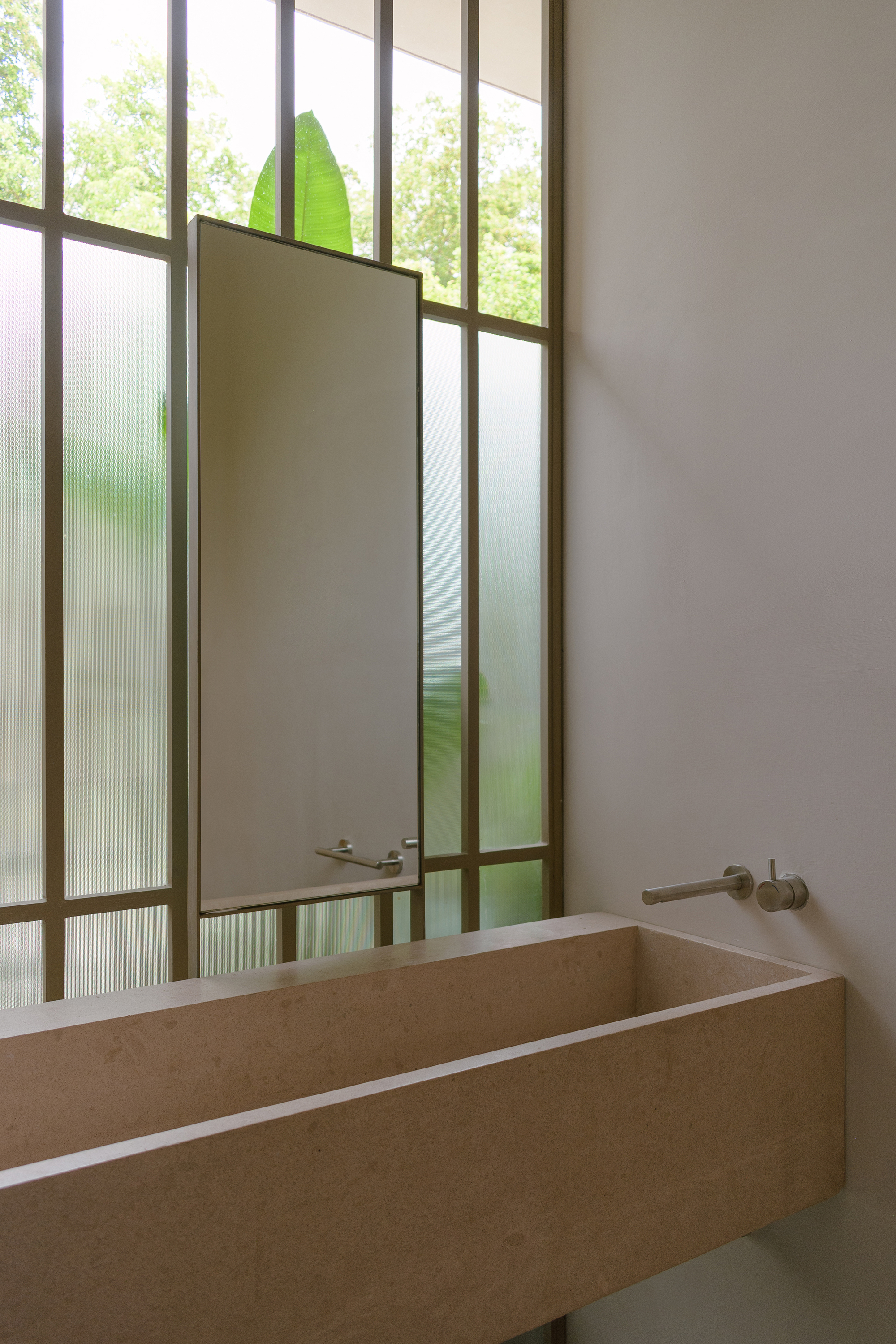 Bathroom with stone sink and steel-framed translucent glass partition revealing green foliage beyond