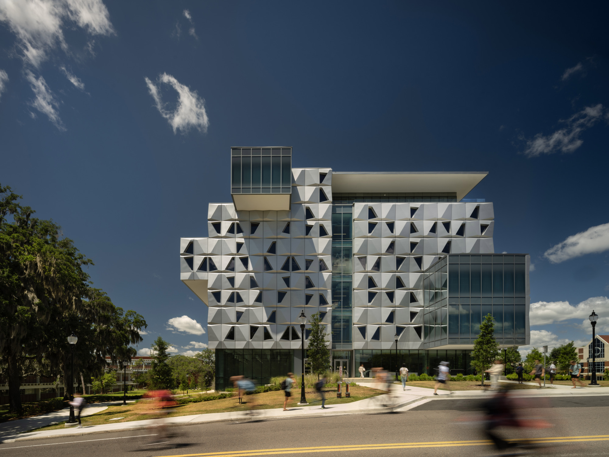 Street corner view showing the stacked volumes with patterned facade panels as pedestrians cross in motion blur