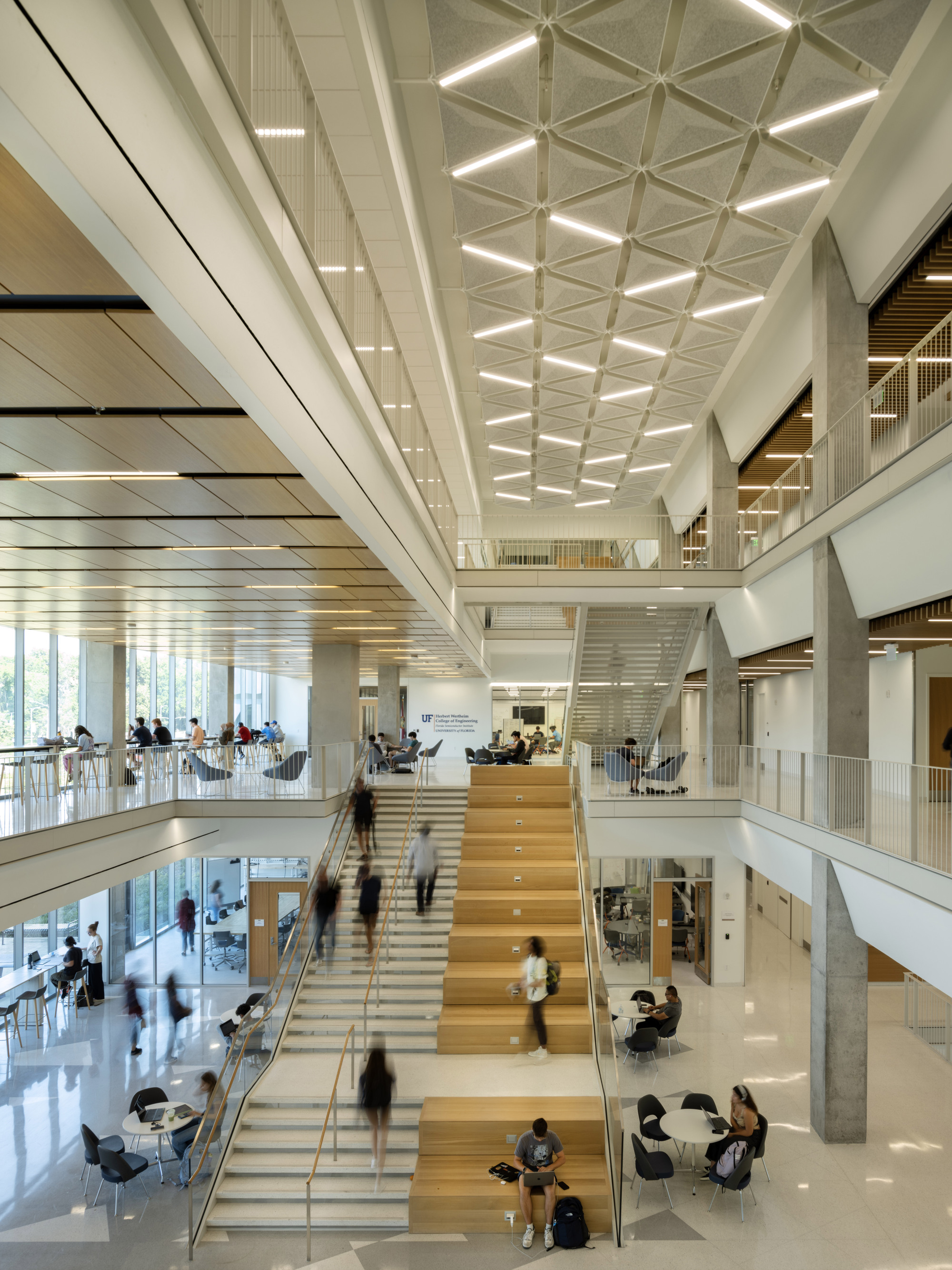 Wide timber staircase with integrated seating beneath a coffered white ceiling and occupied by students