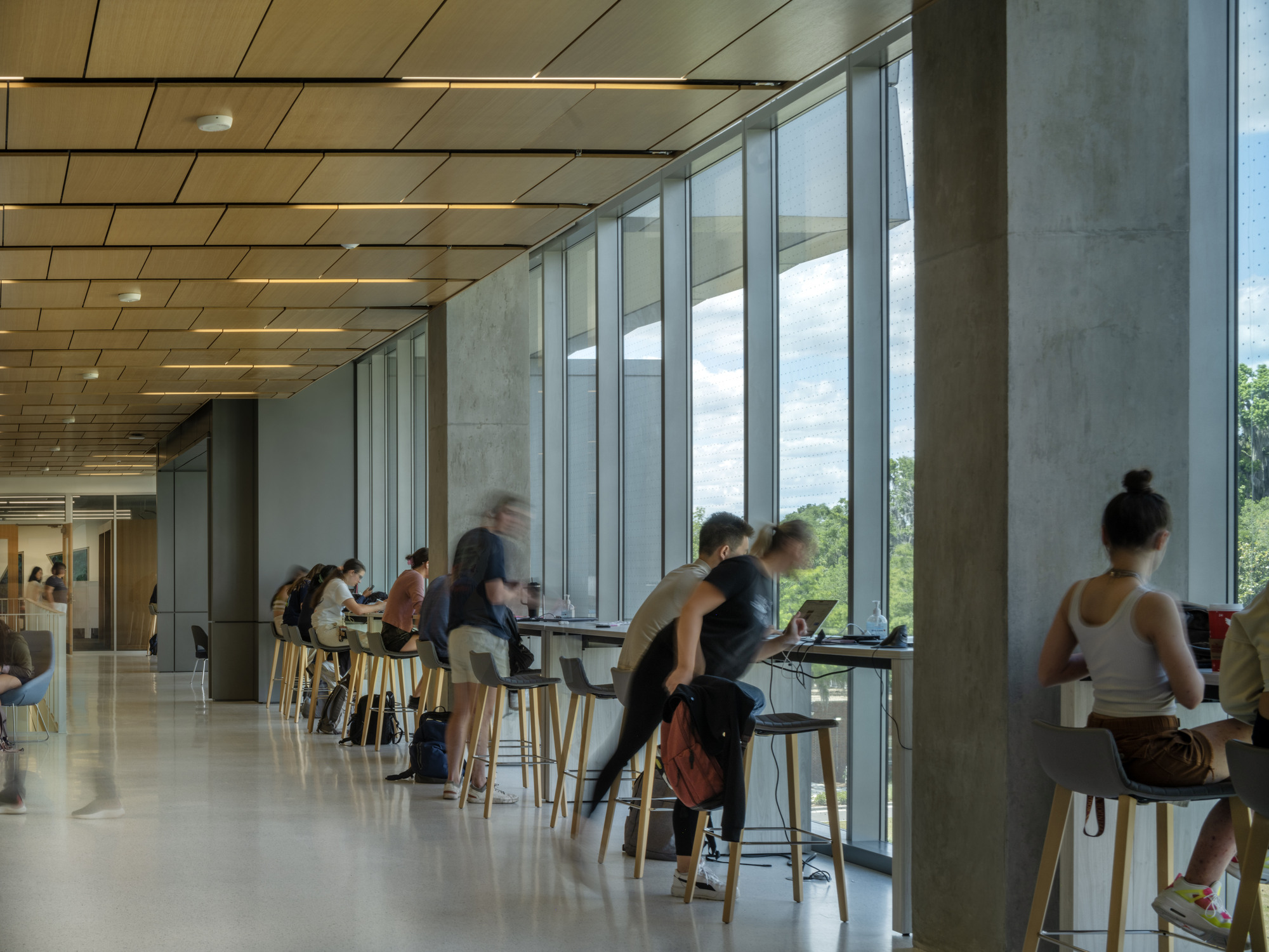 High counter seating along a glazed wall with concrete columns and wood ceiling panels overhead