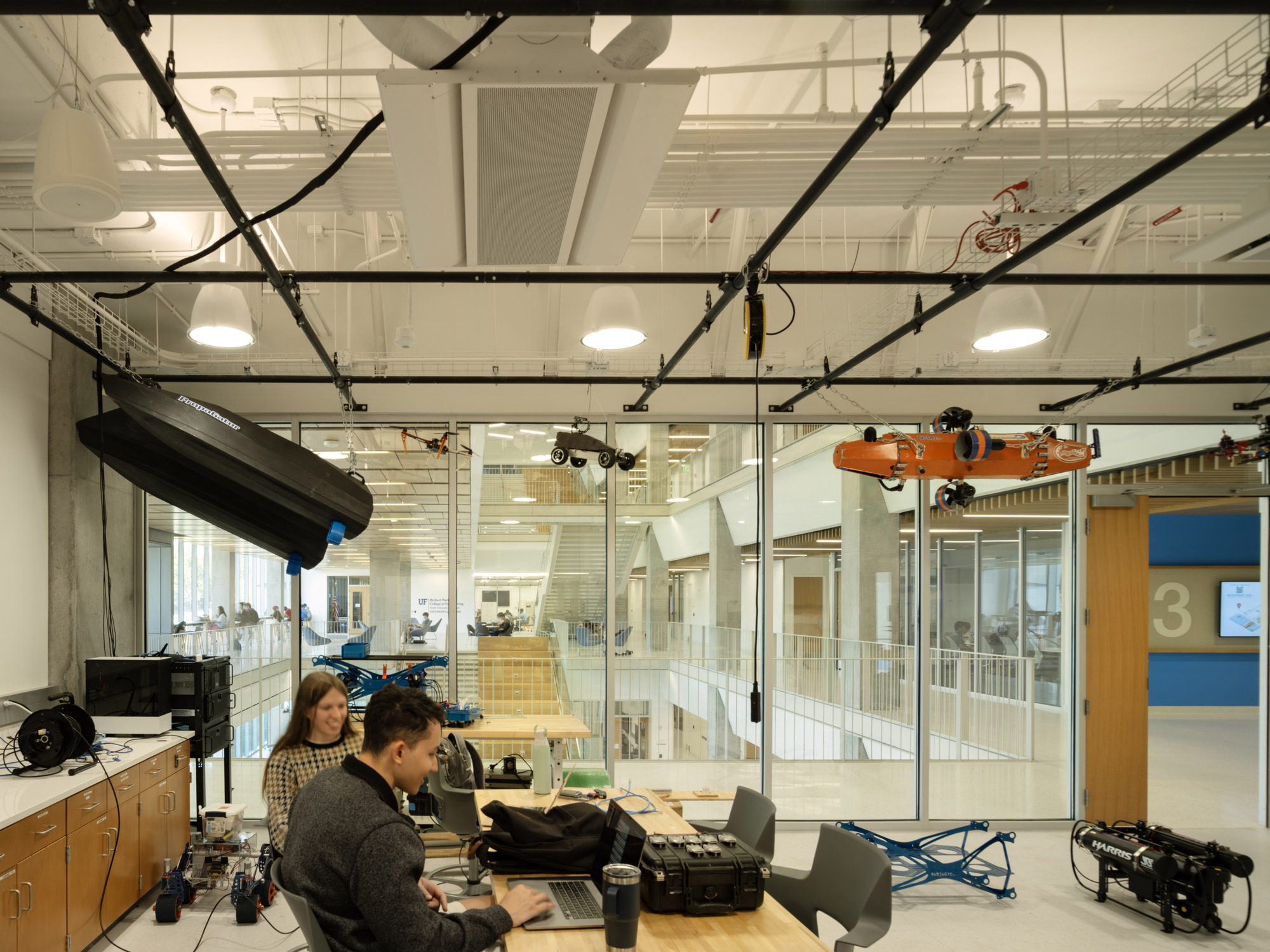 Media production workstation with exposed black conduits and glass partitions overlooking the multi-level atrium