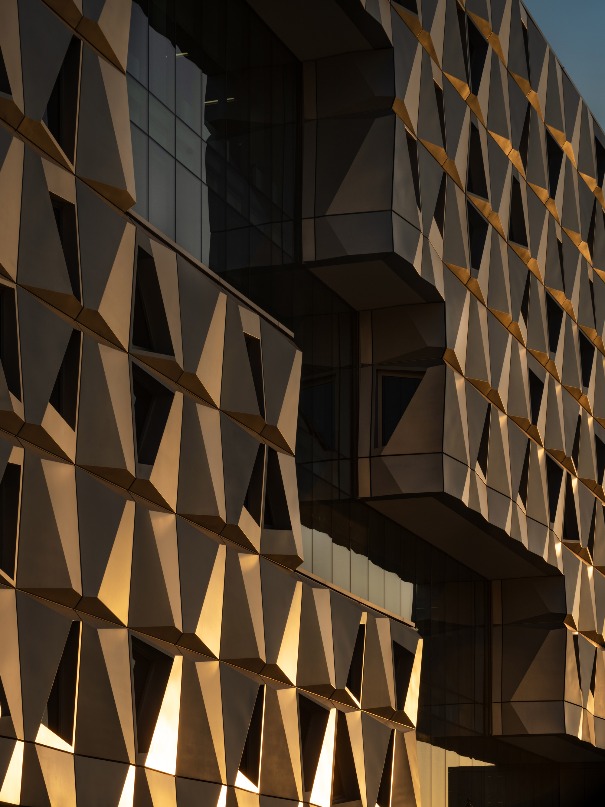 Close-up of triangulated metal panel system catching warm light at sunset across the facade