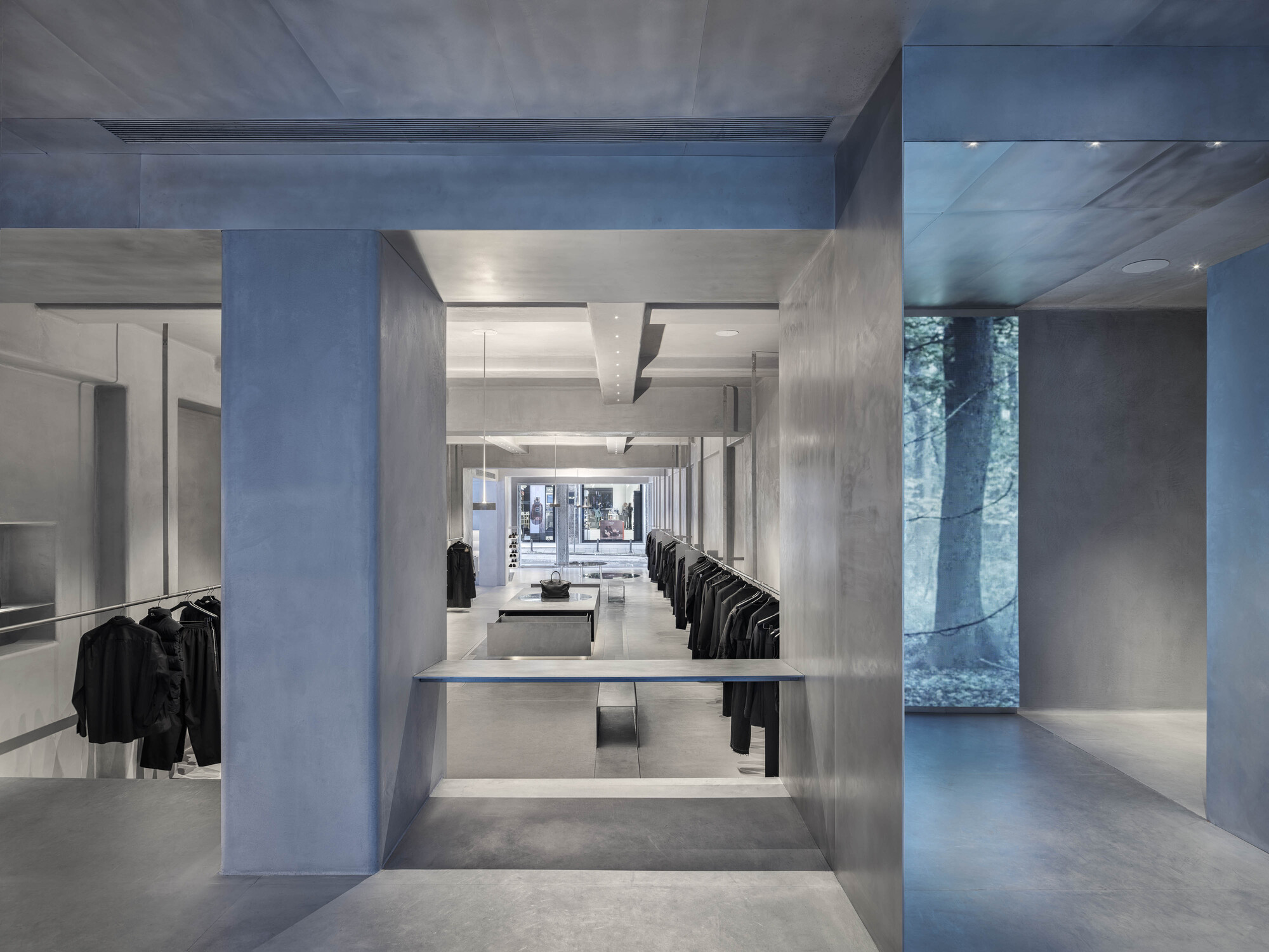 Long interior view through concrete portal showing recessed display tables and clothing racks
