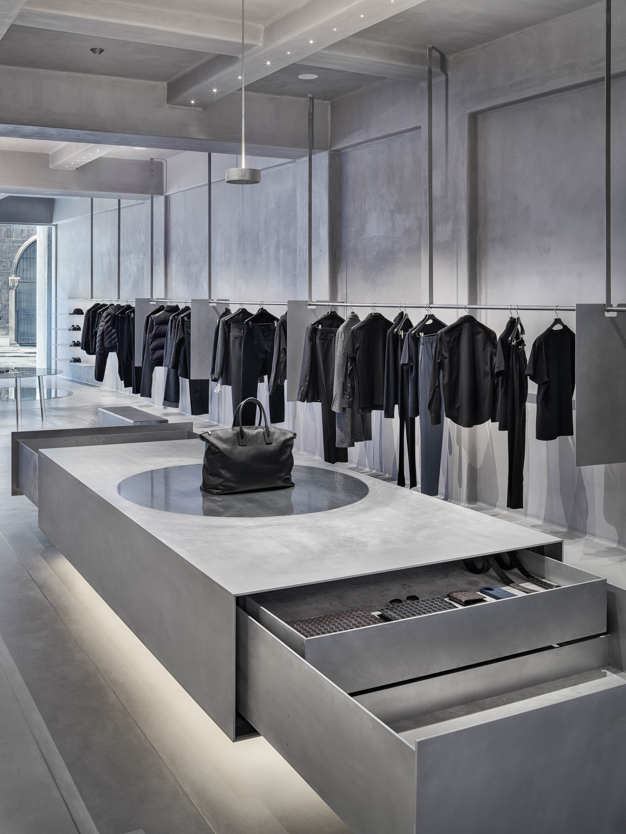 Concrete display counter with open drawer and circular inset beneath hanging garments