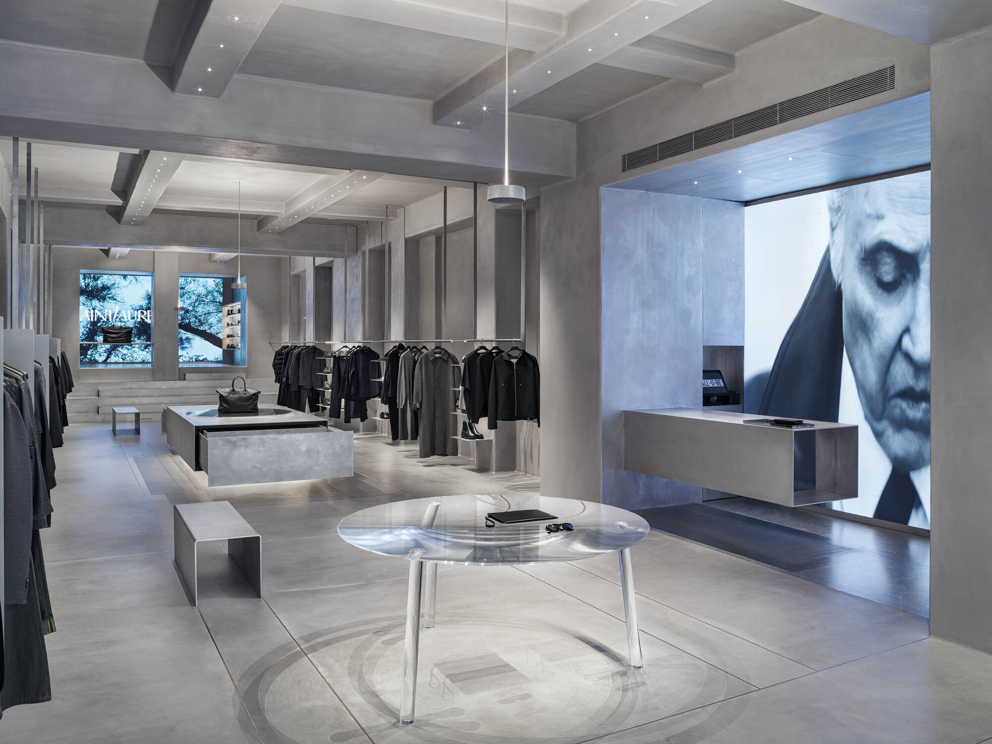 Retail interior with exposed concrete beams, clothing racks and backlit screen with projected imagery