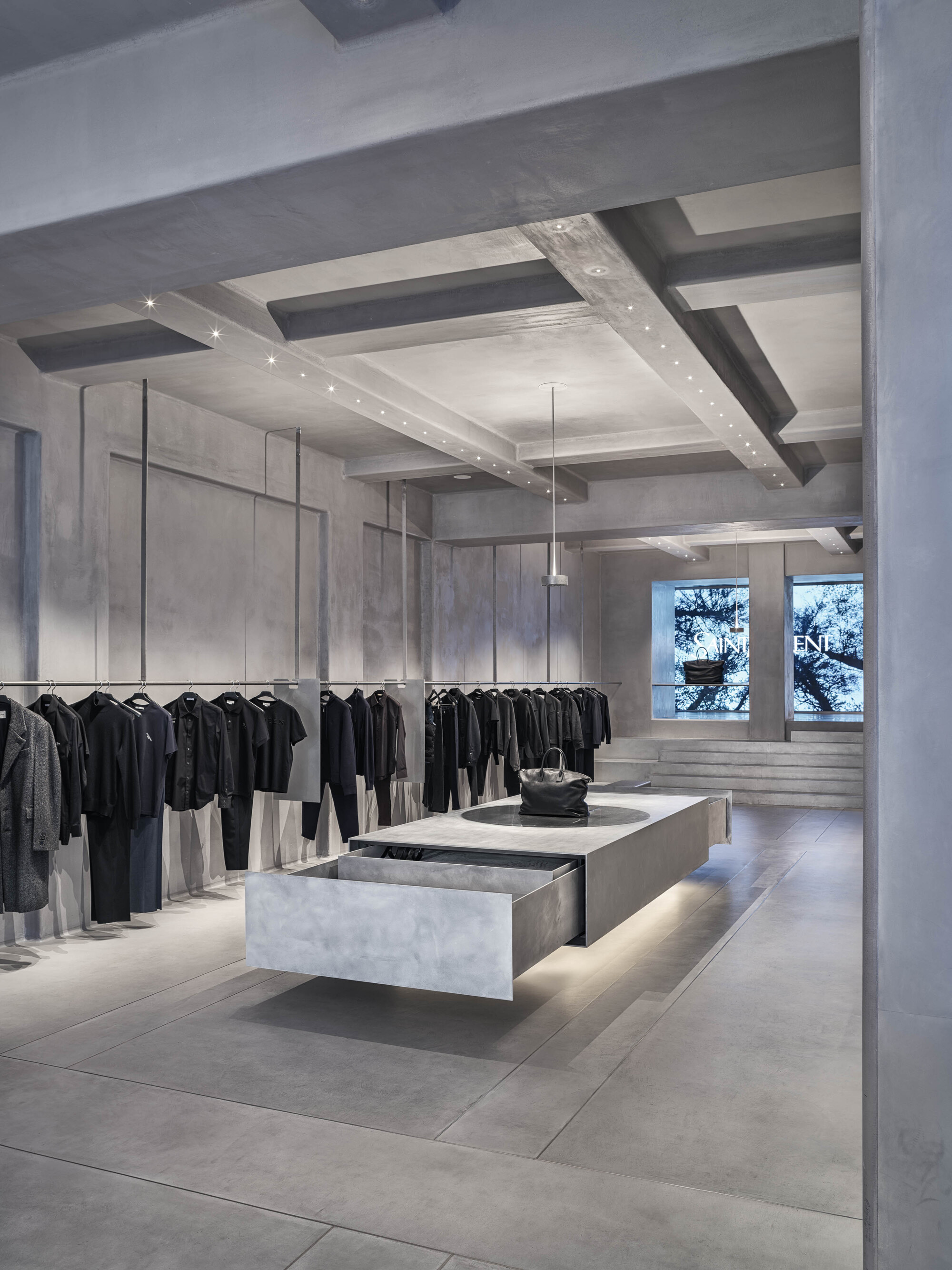 Concrete coffered ceiling with recessed lighting above clothing display and windows overlooking trees