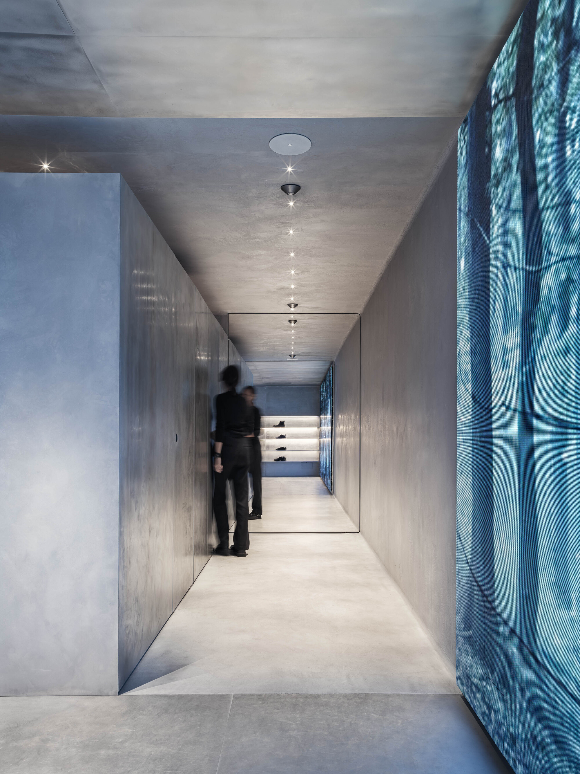 Narrow corridor with polished concrete walls, suspended ceiling lights and a person in motion