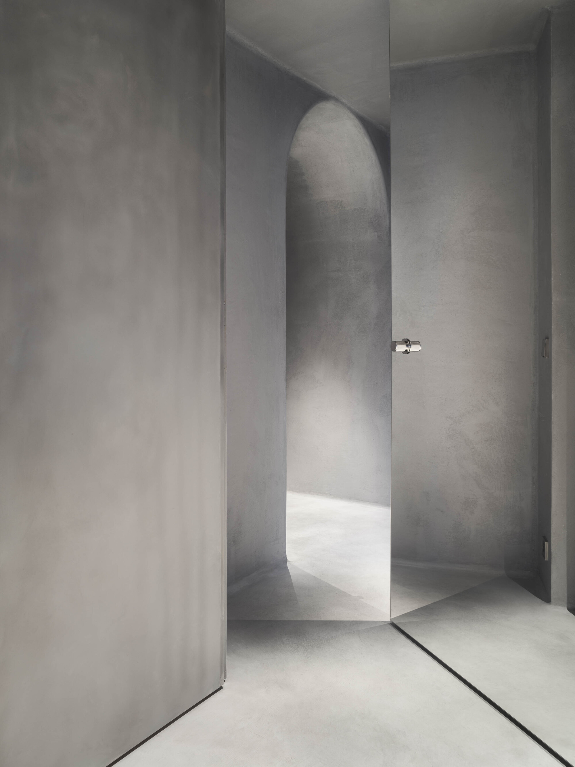 Arched passageway in smooth plaster with chrome door handle and soft natural light