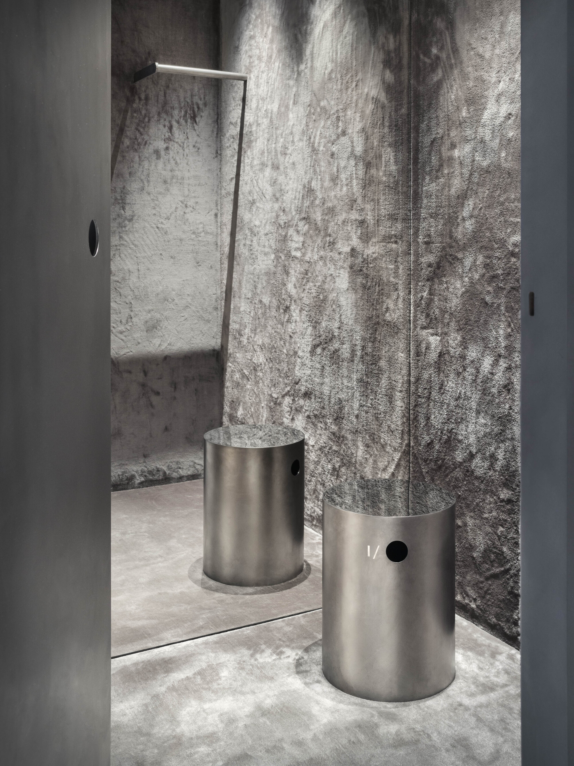 Fitting room entrance with textured silver wall panels and two cylindrical steel seating elements
