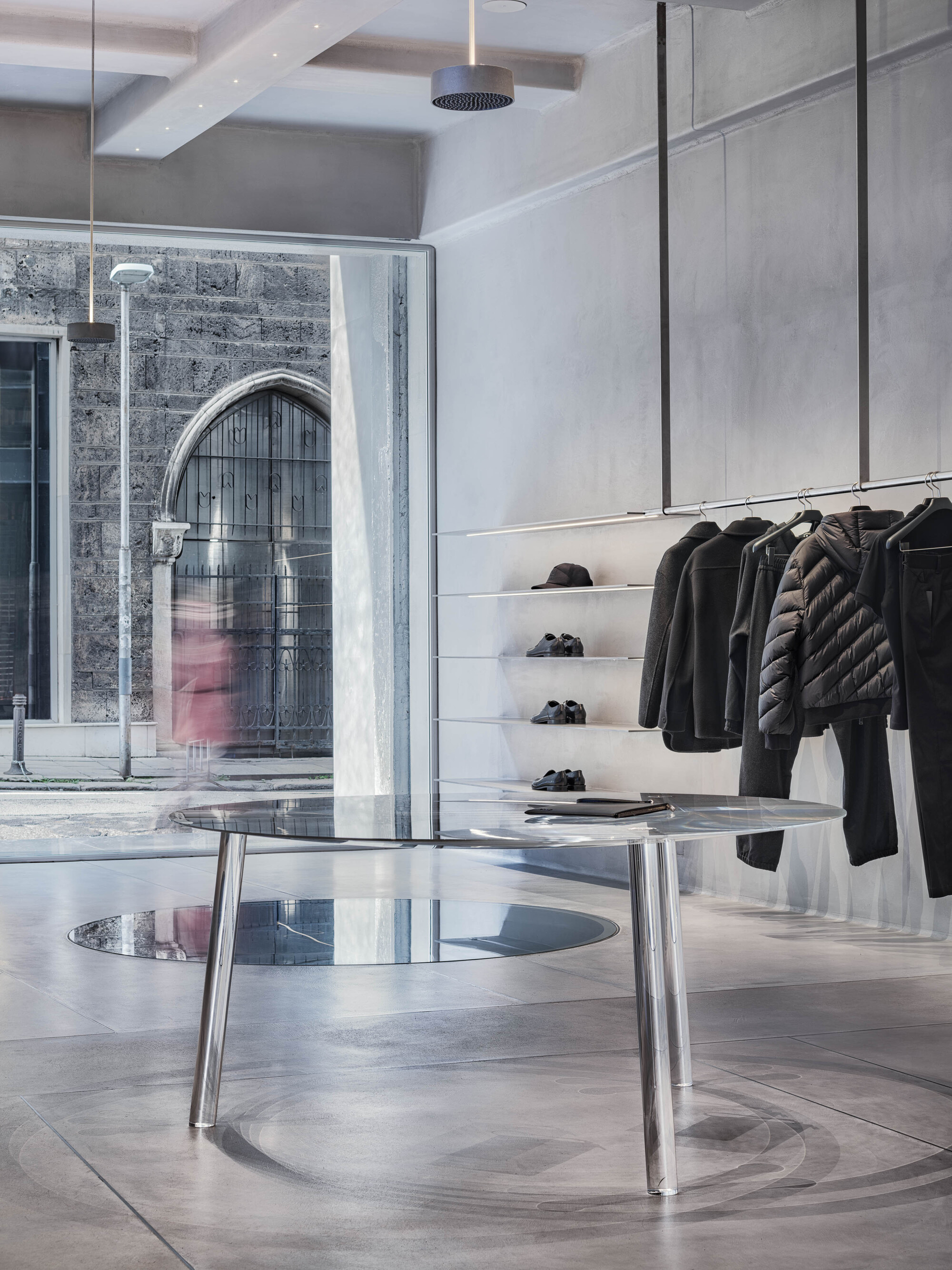 Glass storefront revealing an arched brick facade with a person passing in pink clothing