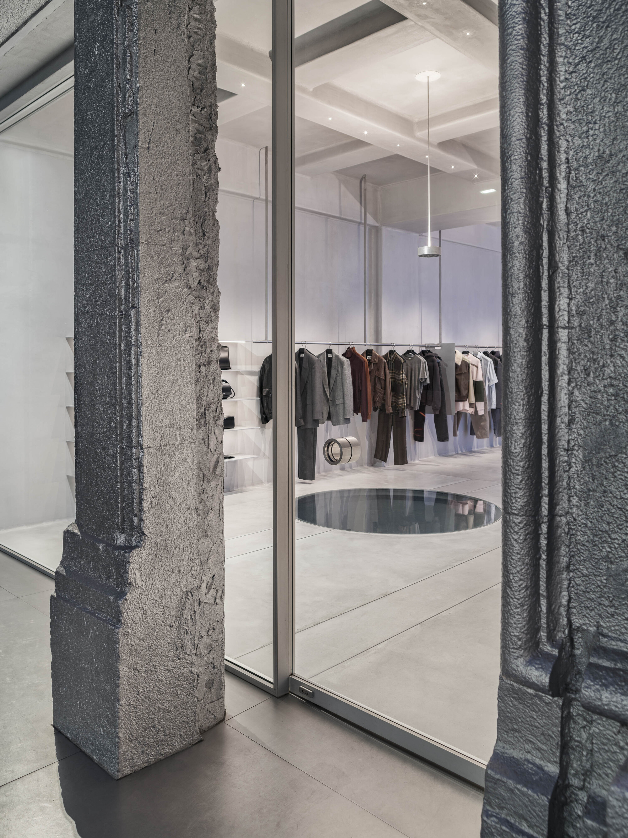 Charcoal-painted concrete column beside a glass door threshold looking into a retail space