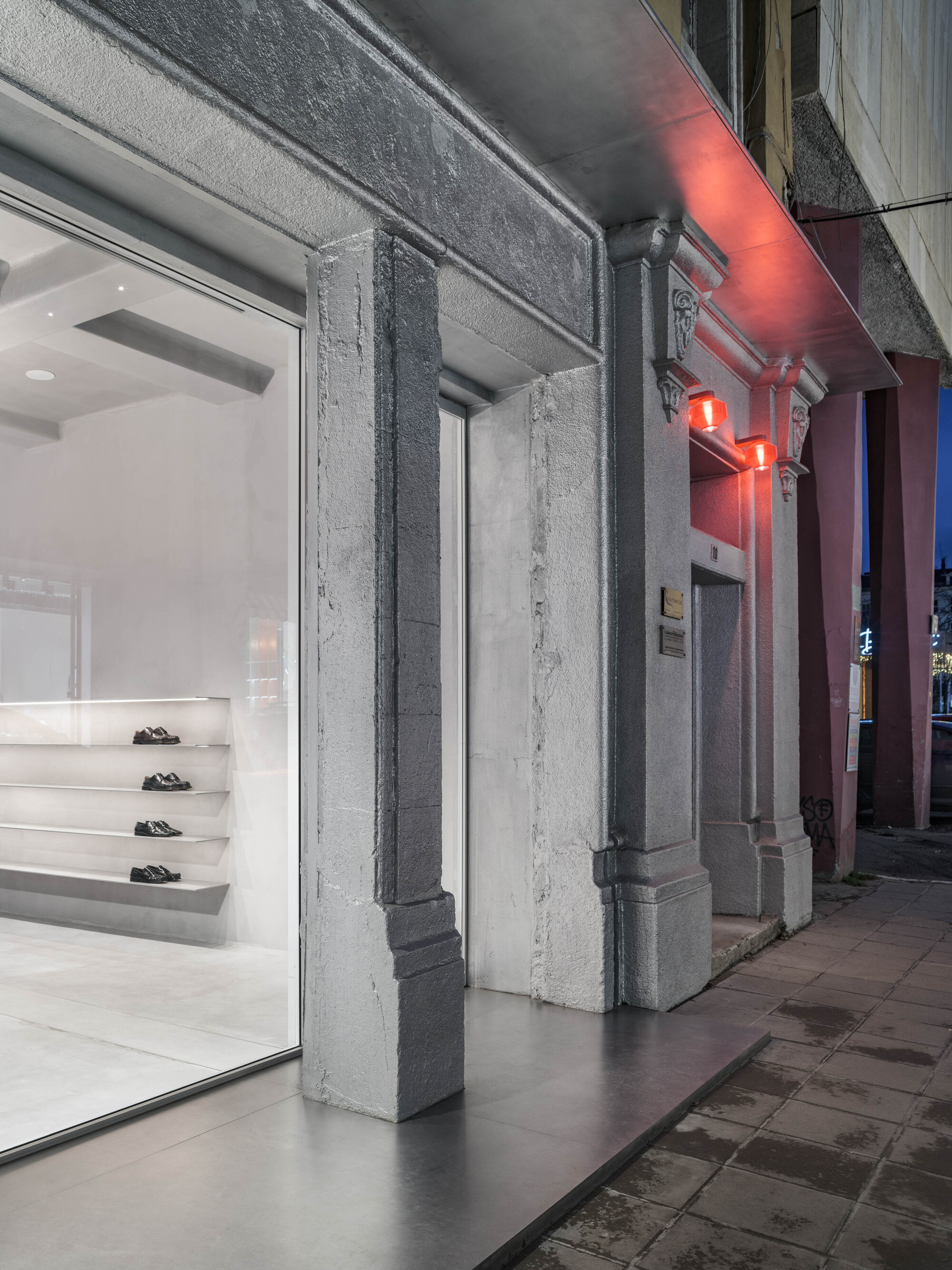 Exposed concrete columns beneath red neon lighting along the exterior storefront at dusk