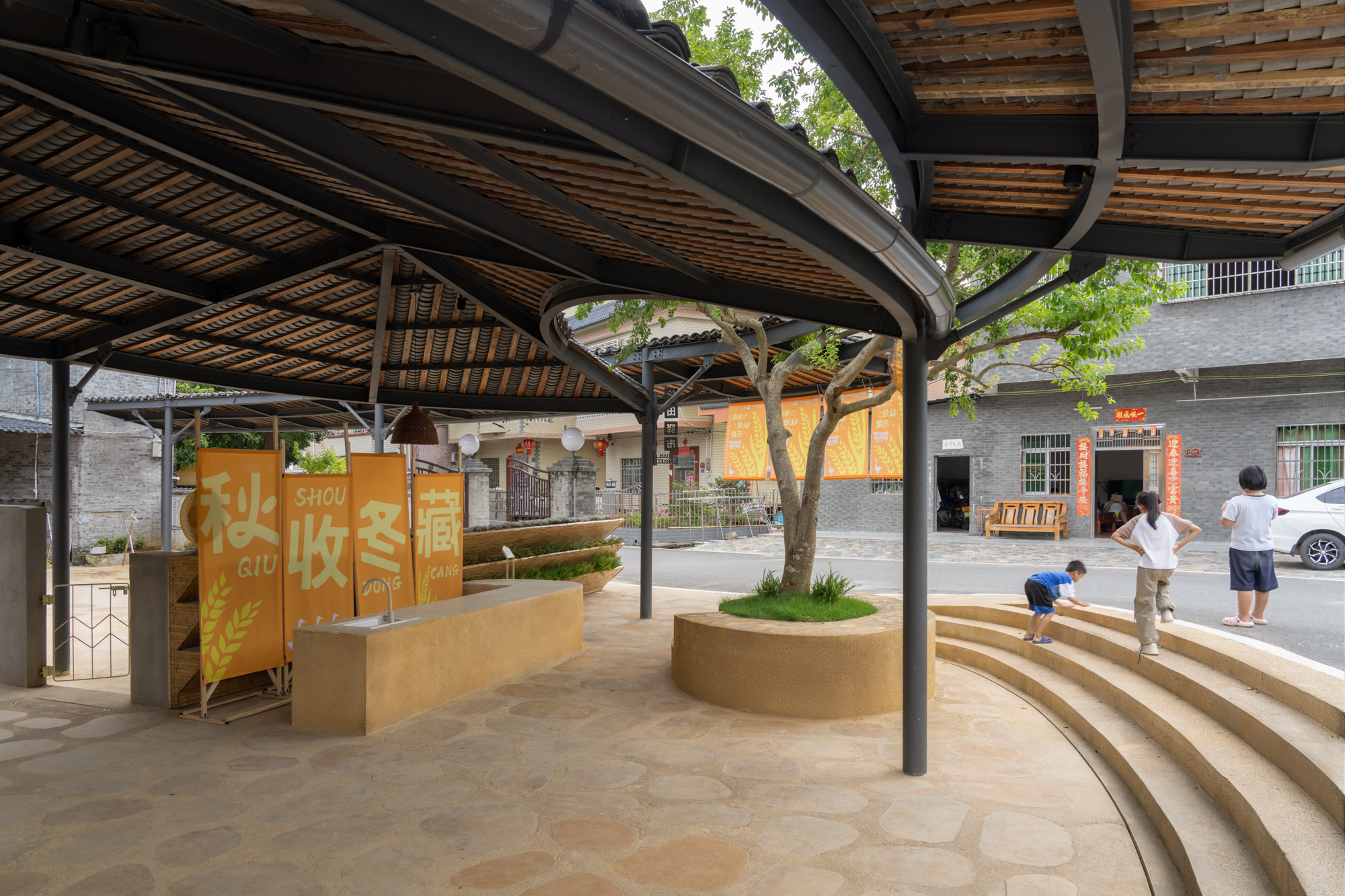 Curved timber steps with integrated planters beneath a pavilion roof with steel columns and bamboo ceiling structure