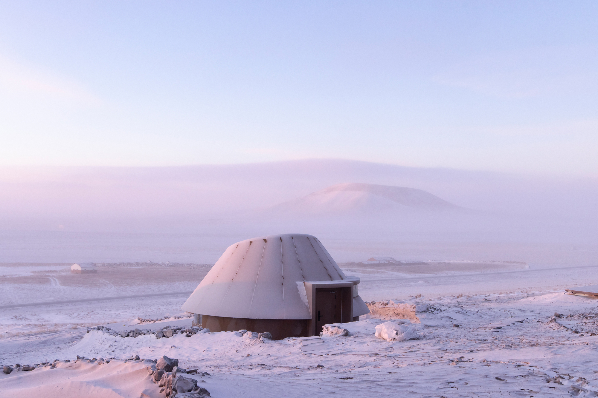 Single dome shelter with rectangular entrance volume set against a distant snow-covered mountain