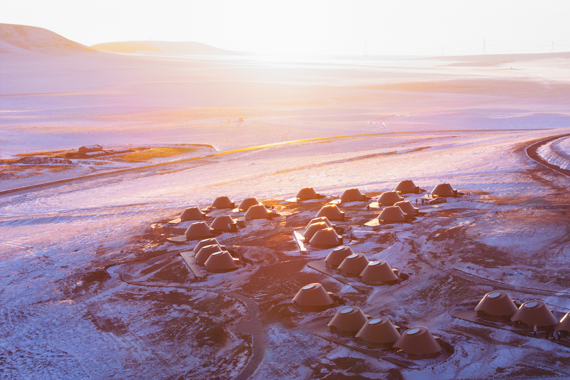 Oblique aerial view of dome shelters arranged in organic clusters across a snow-dusted plain at sunset