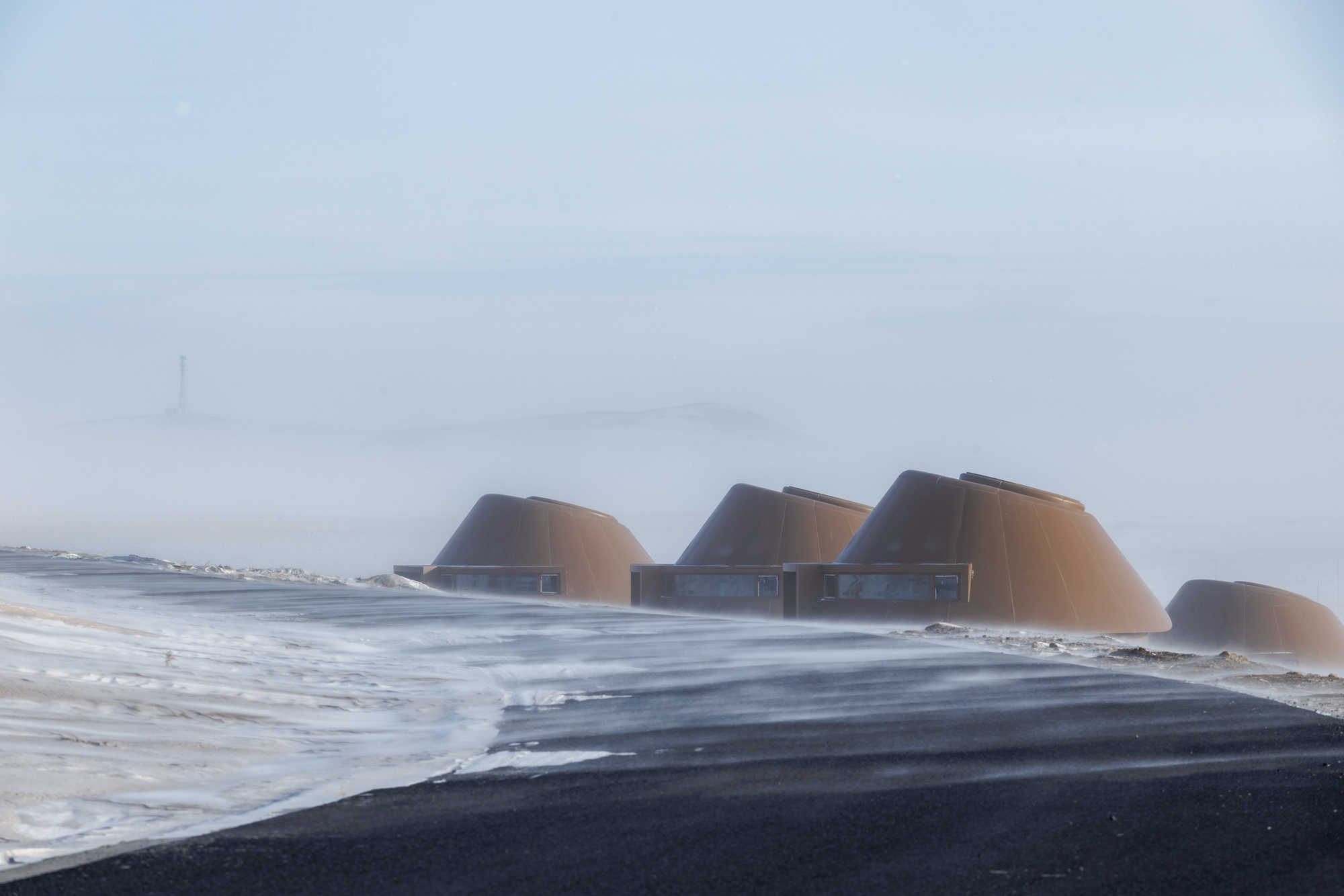 Row of dome-roofed structures with glazed facades emerging from drifting snow in heavy fog