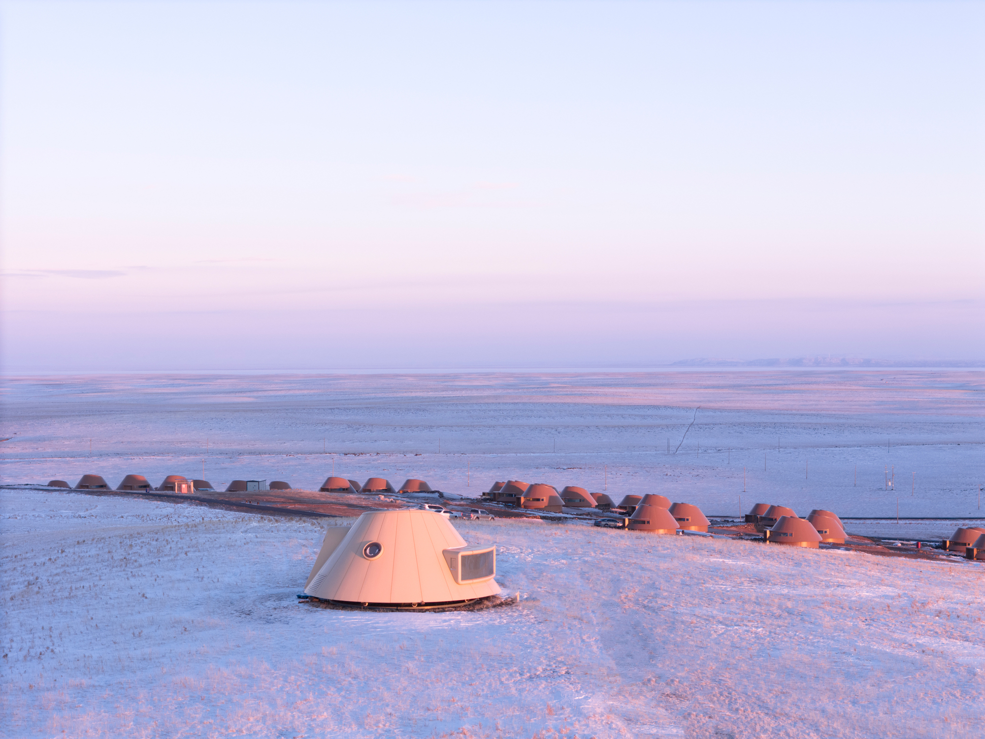 Single dome shelter with porthole window and rectangular opening standing in snowfield at dawn