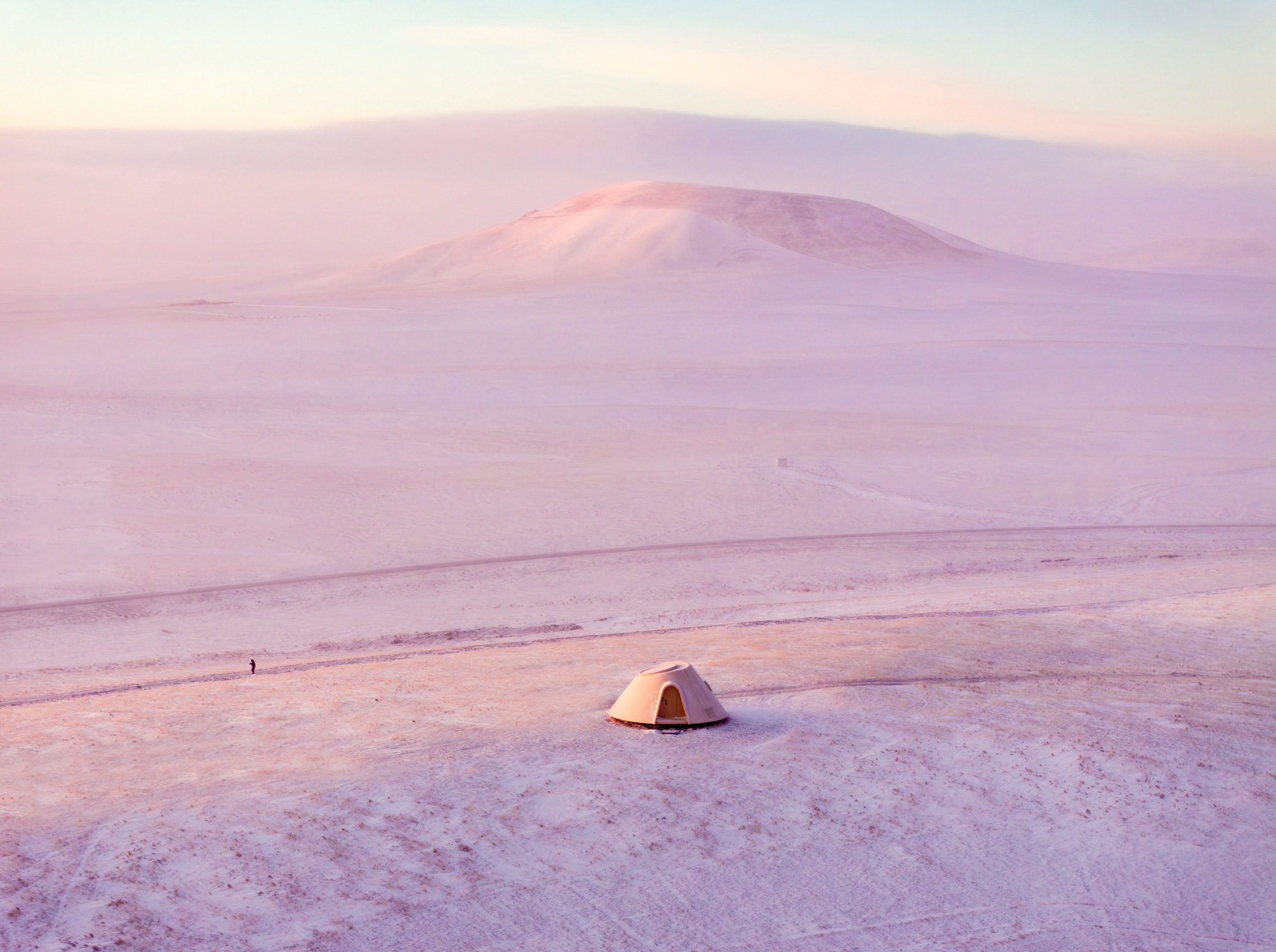 Solitary dome structure in foreground with distant figure and snow-covered hill in soft twilight