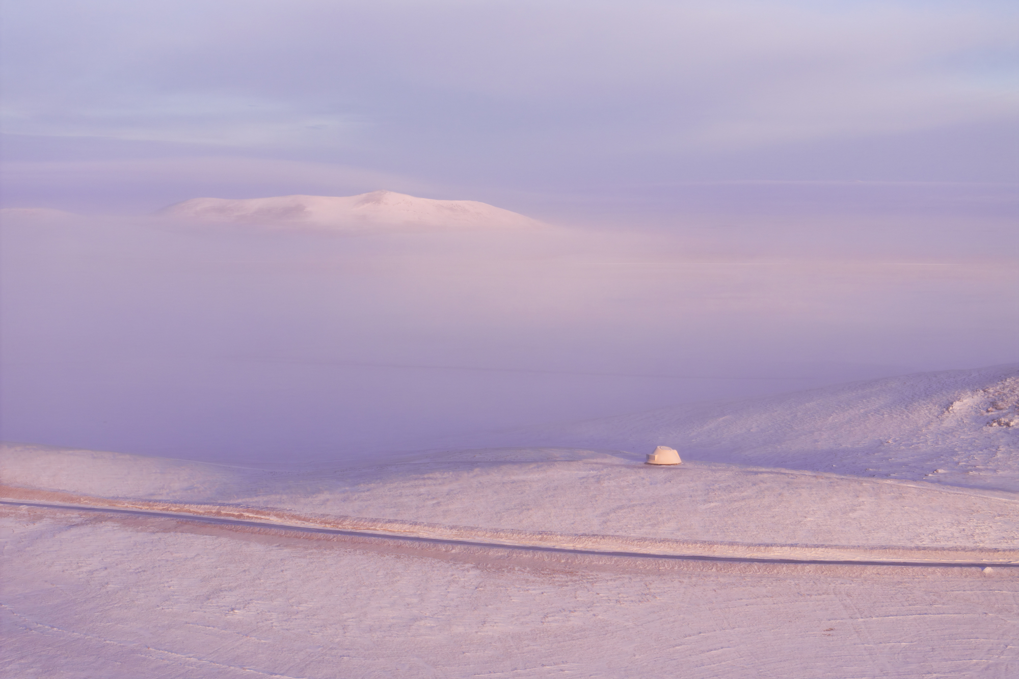 Dome shelter set in snowy valley with rolling hills and low cloud cover at dusk