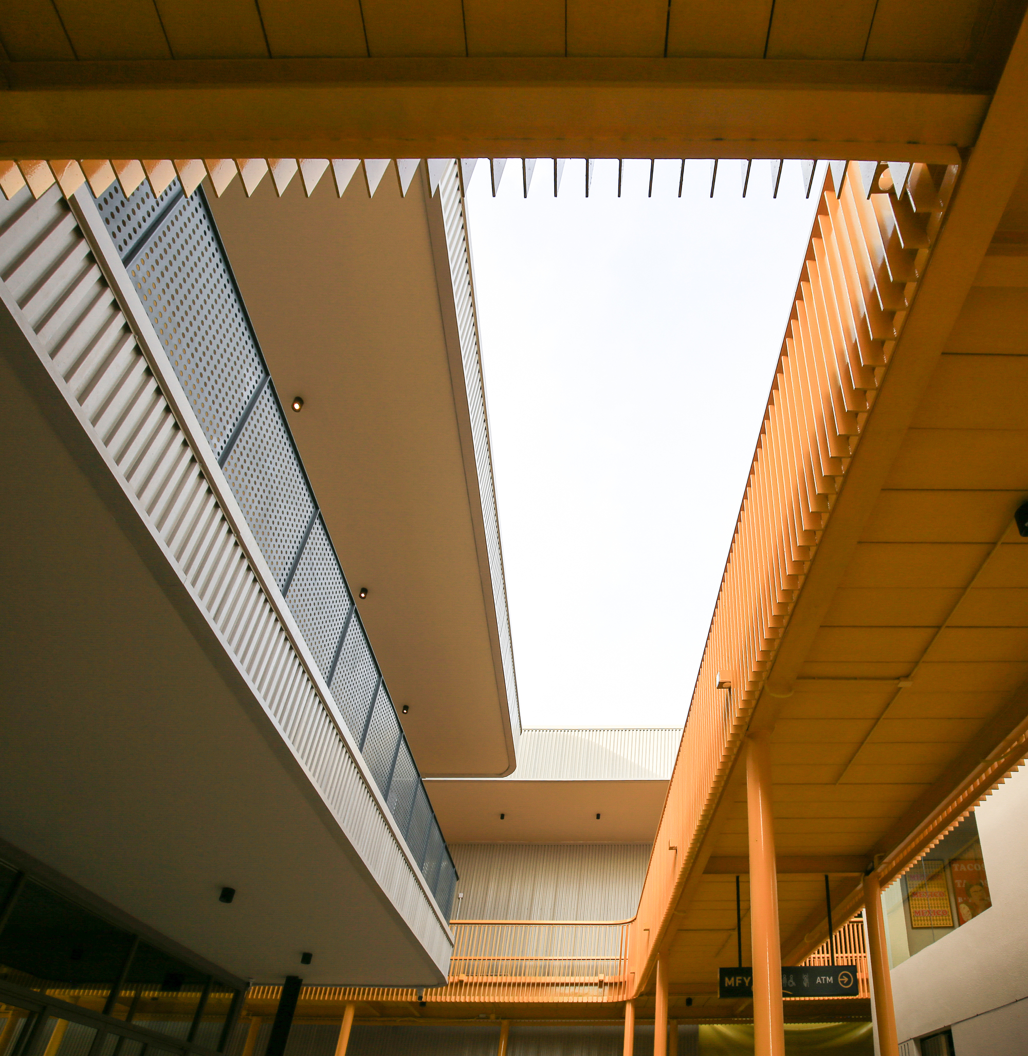 Interior courtyard looking up at rectangular skylight framed by timber ceiling and corrugated metal