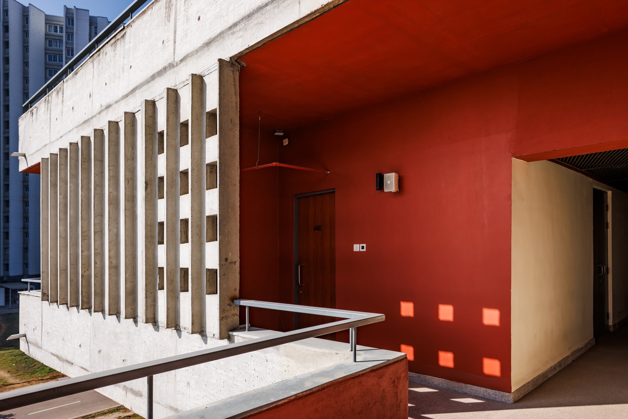 Concrete brise-soleil screen wall meeting a red-painted wall at a doorway