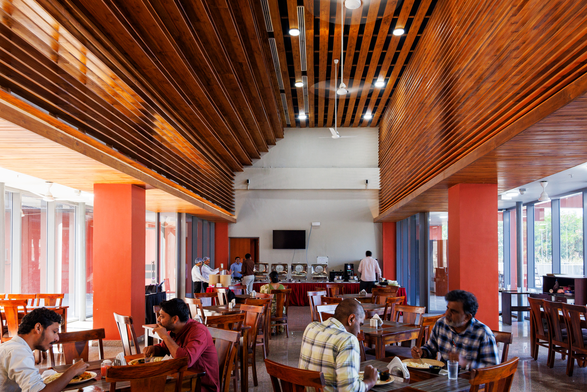 Dining hall with timber-slatted ceiling, red columns and rows of wooden tables