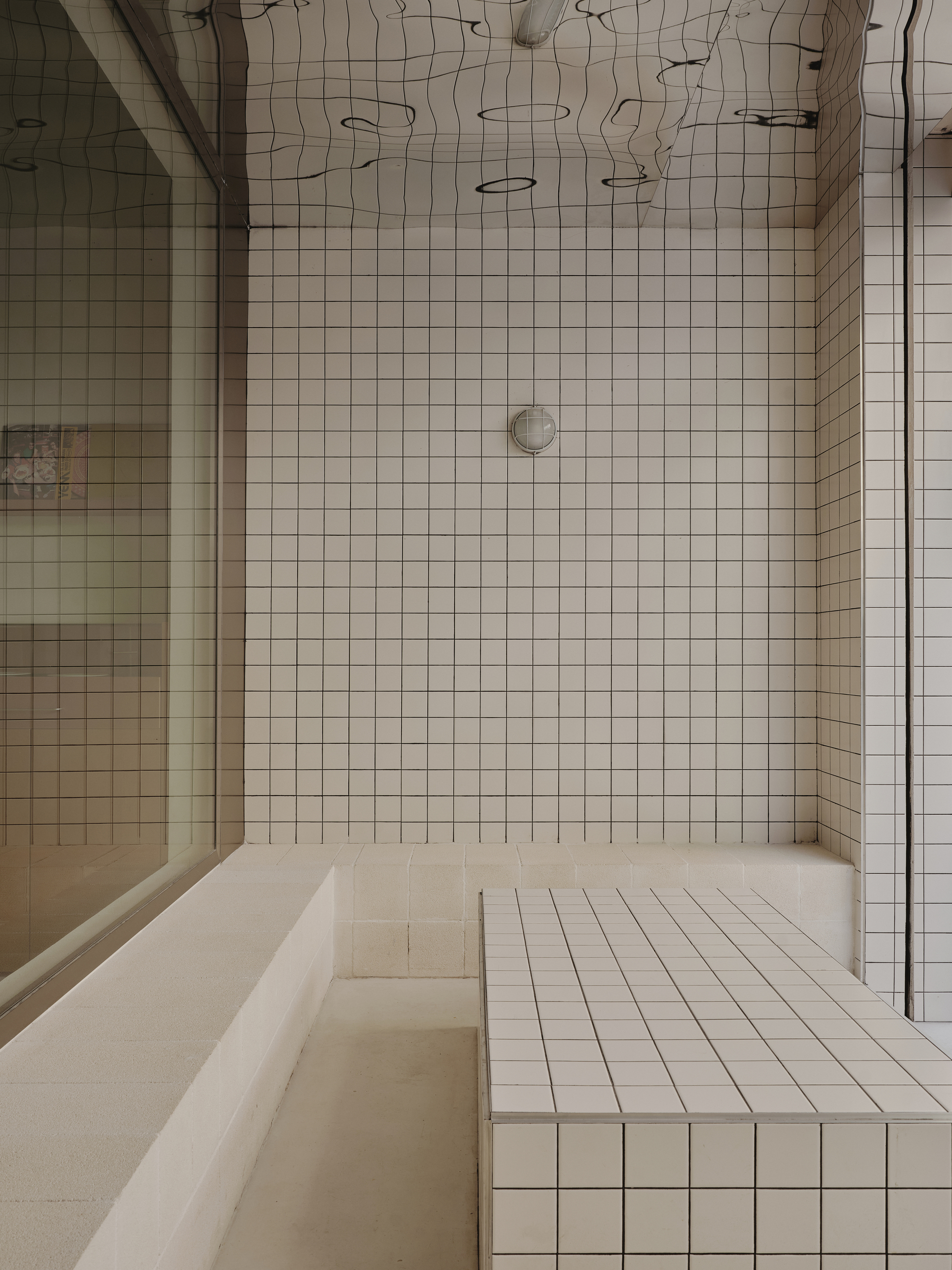 Tiled shower enclosure with built-in bench and white grid ceramic walls beneath exposed ceiling joinery
