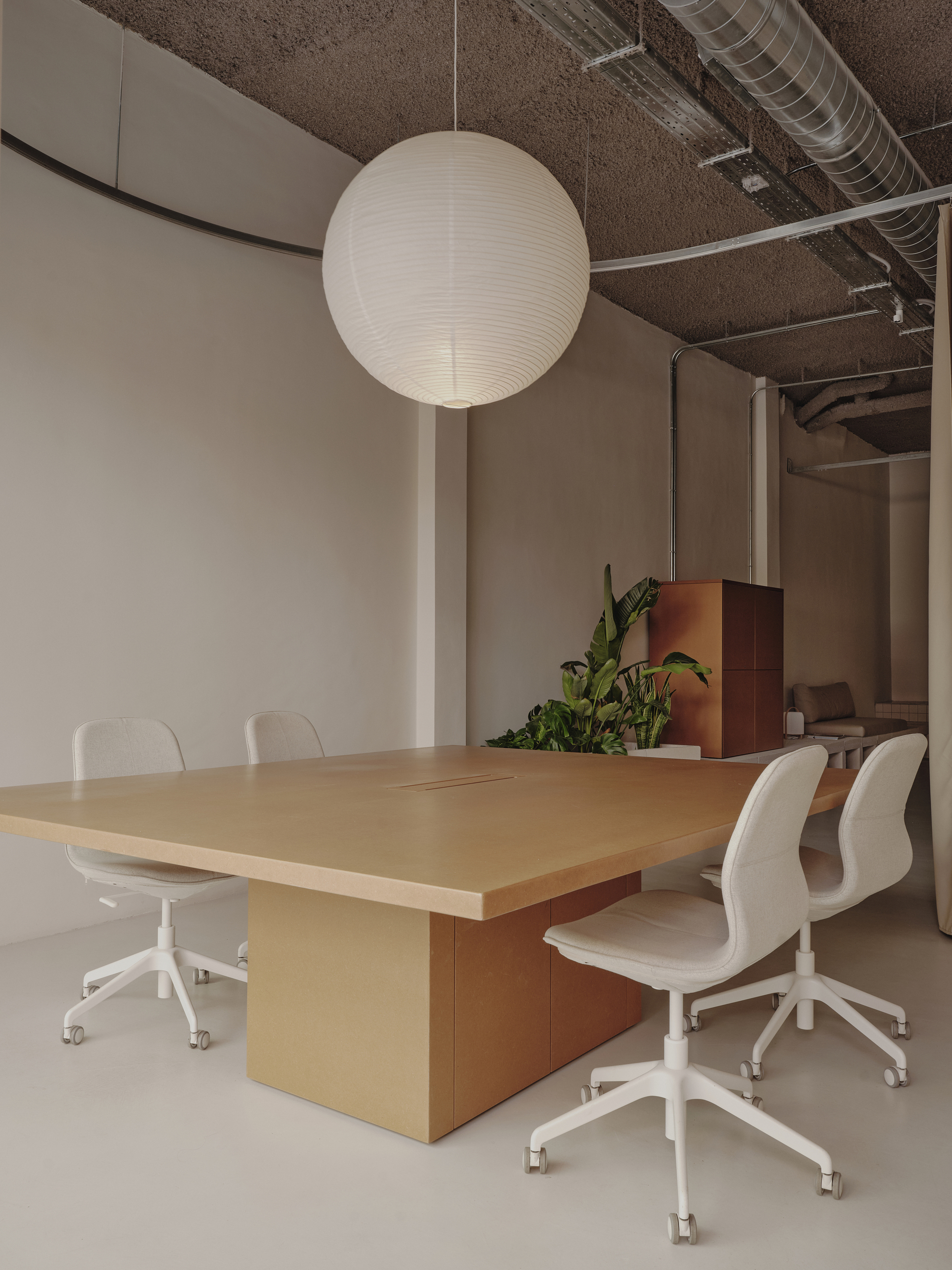 Conference table with timber pedestal base beneath a sphere pendant and exposed textured ceiling with ventilation ductwork