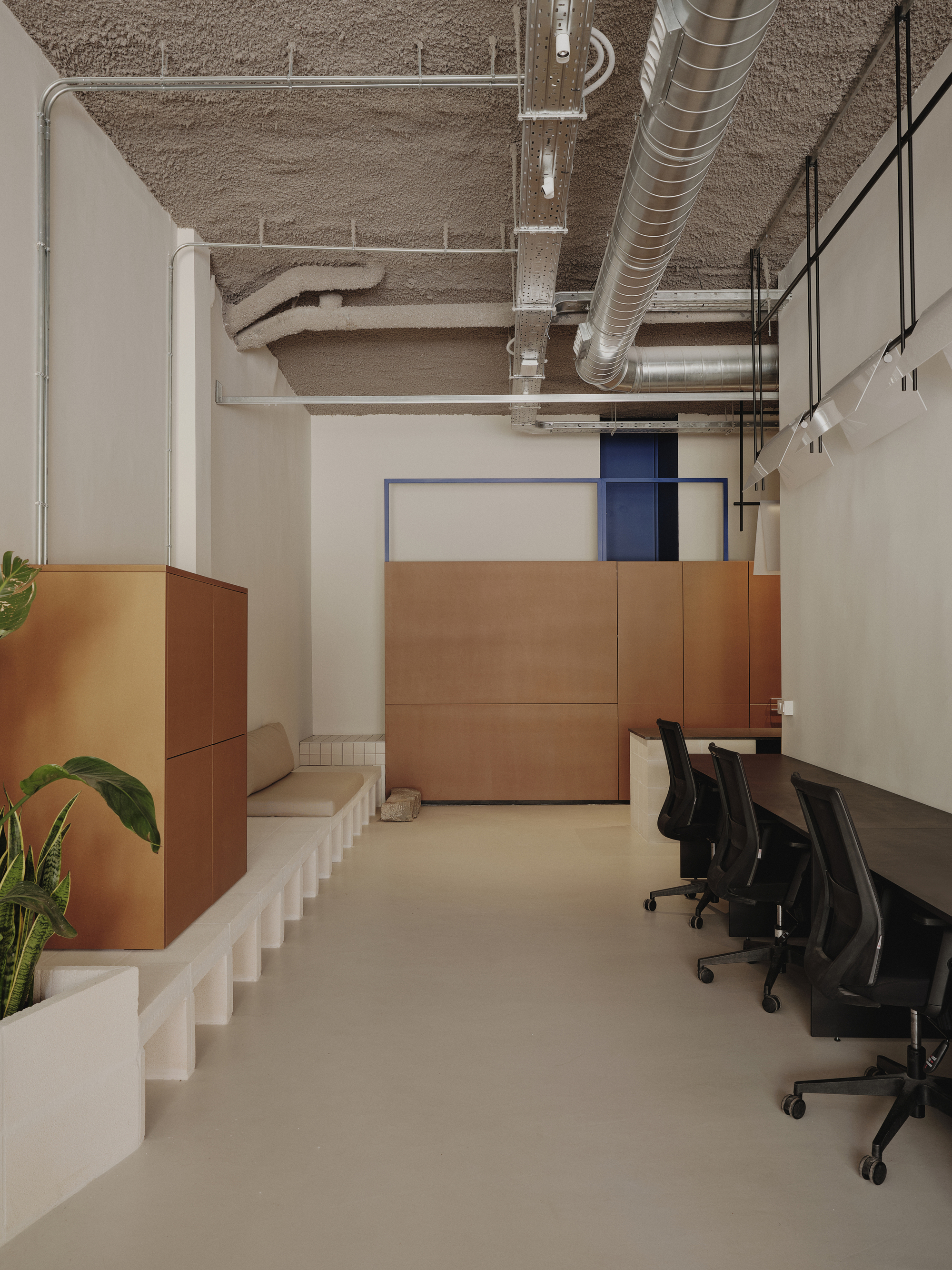Office space showing copper-clad joinery elements, white stepped seating platform, and exposed concrete ceiling with metal ducts