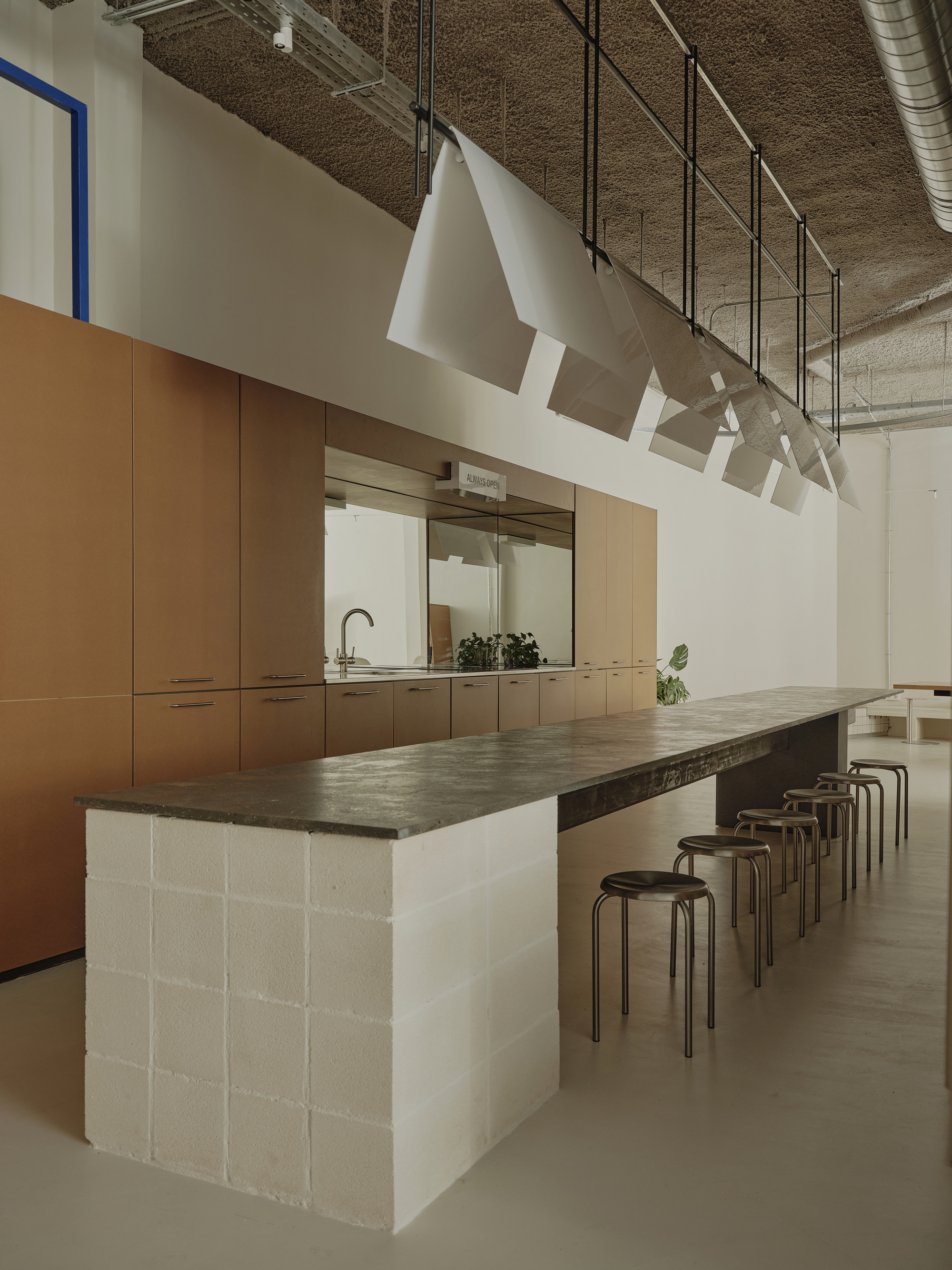 Island table with white concrete block base and timber cabinetry beyond in a space with exposed ductwork