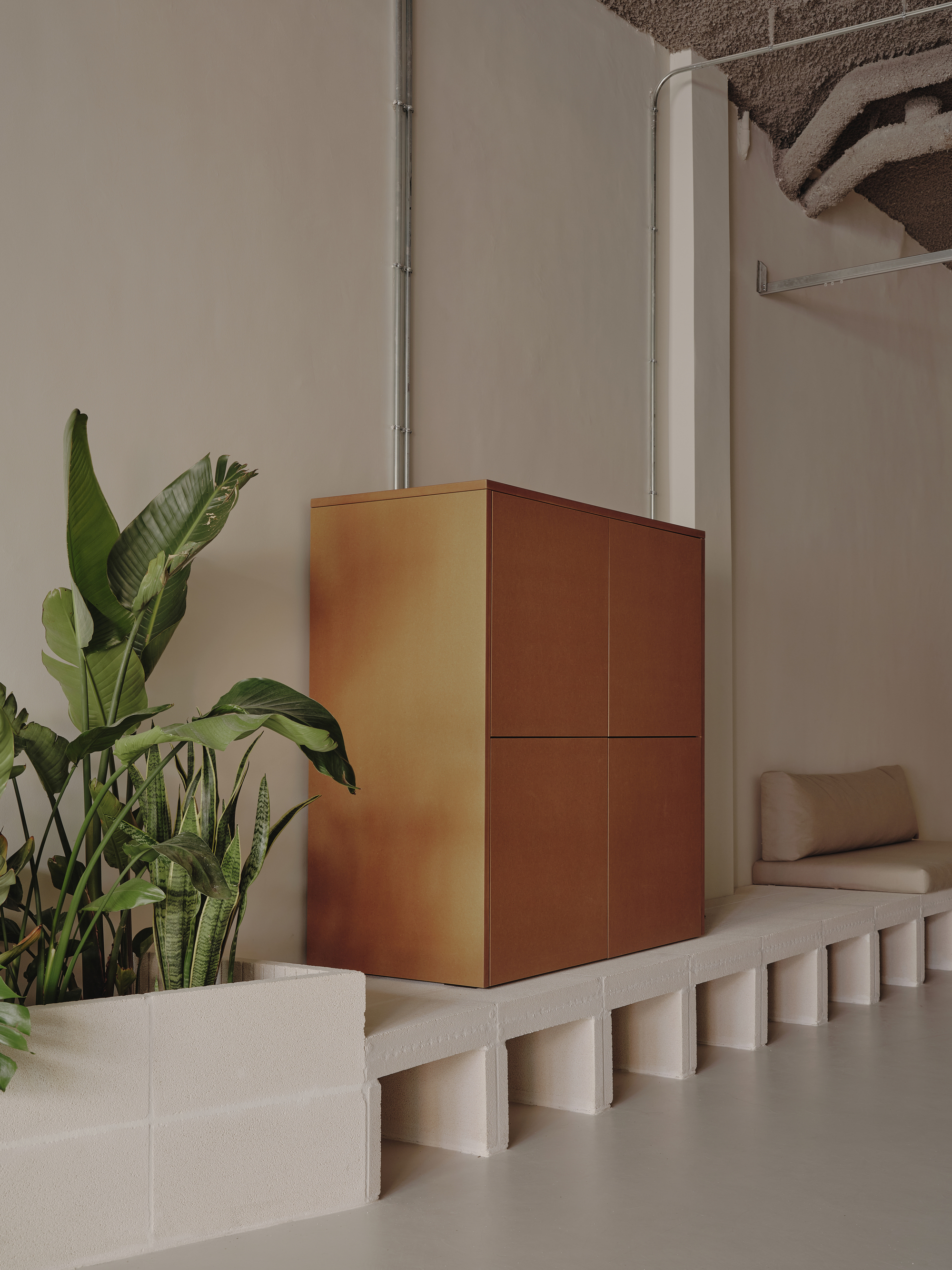 Copper-clad cubic volume on a fluted concrete plinth beside tropical plants and a white column