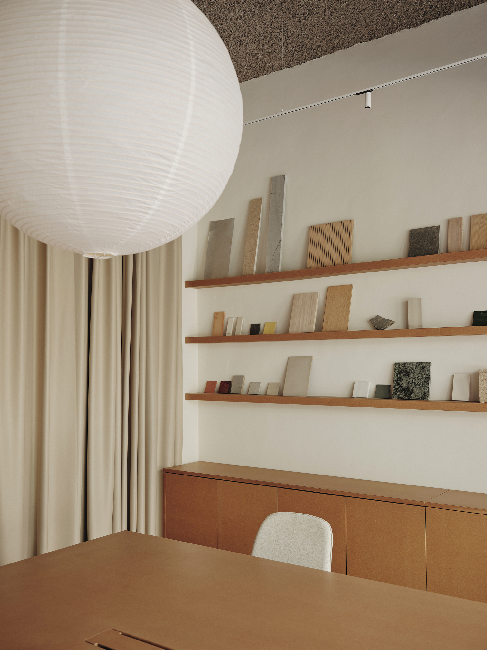 Timber shelving with material samples above a low cabinet and table beneath a spherical paper lantern