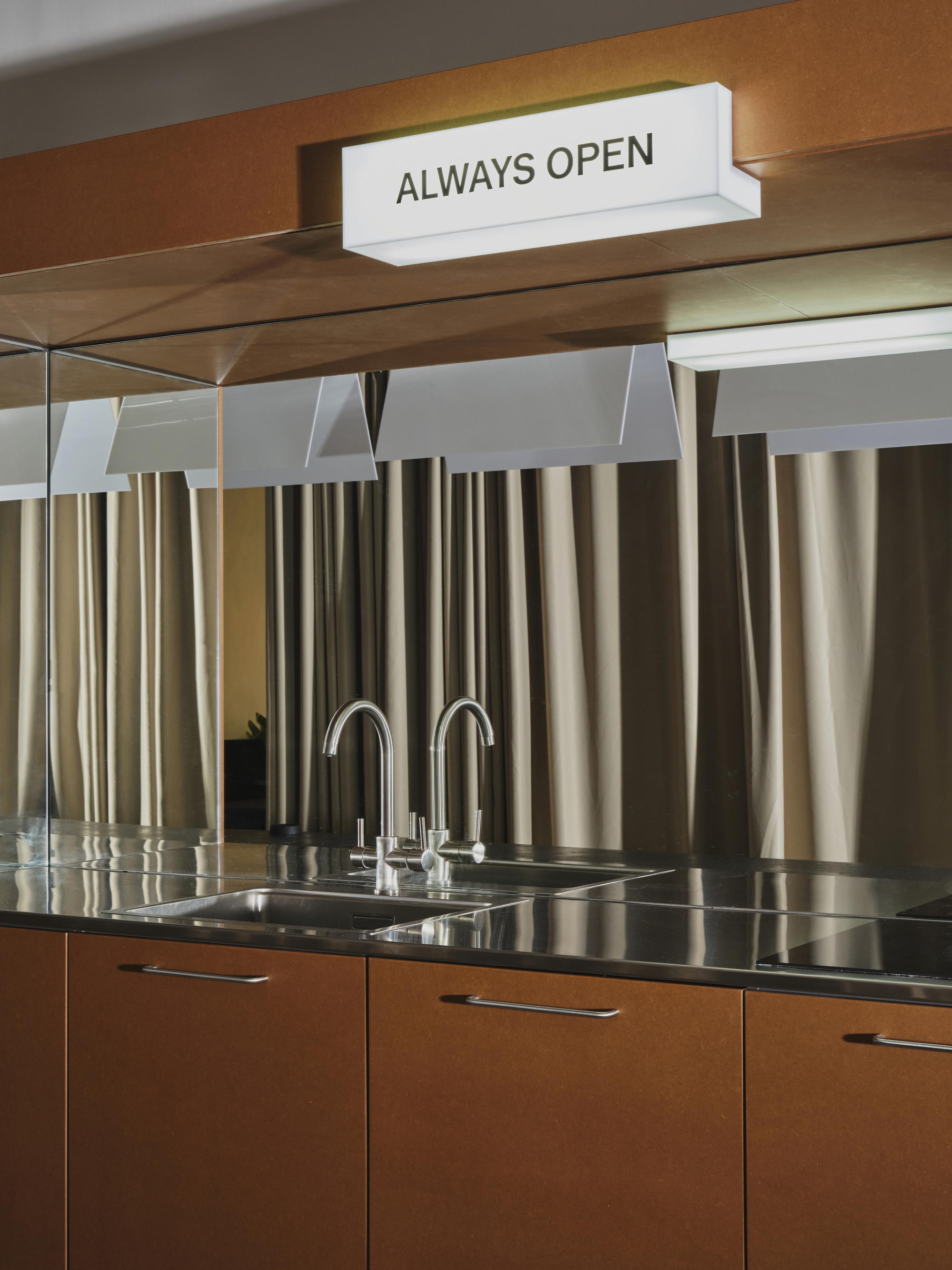 Kitchen counter with stainless steel sink and backsplash of vertical metal tubes beneath timber shelving